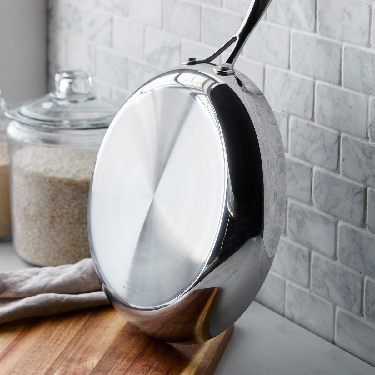 Valencia Pro stainless steel frying pan from an 18-piece cookware set, standing on its side on a wooden cutting board.