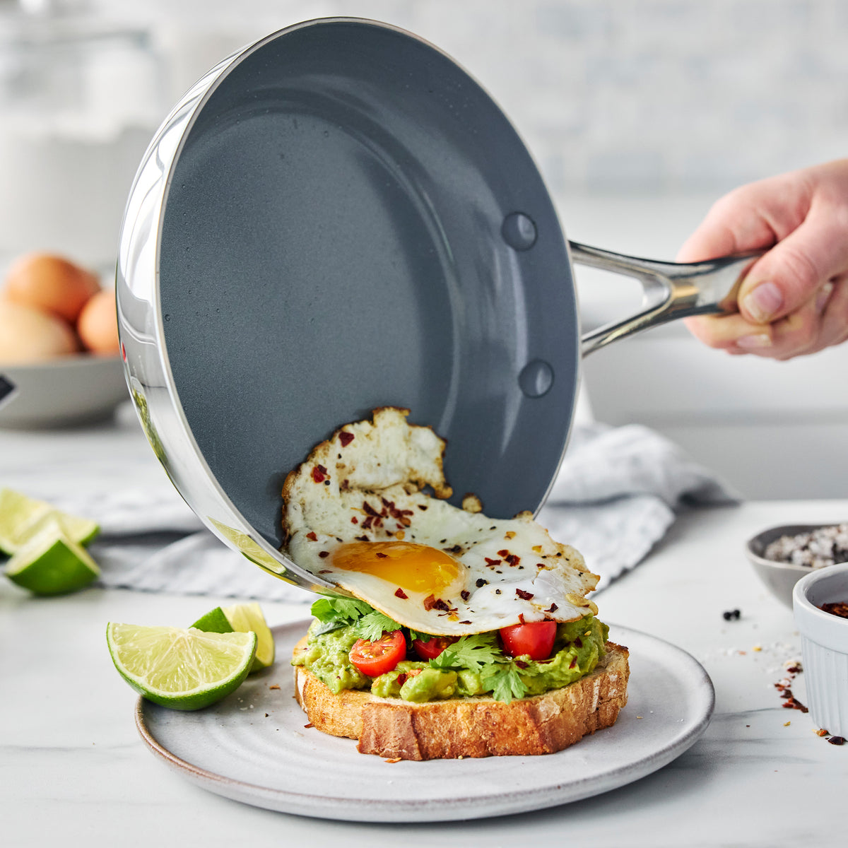 Valencia Pro stainless steel frying pan sliding a fried egg onto avocado toast with cherry tomatoes.
