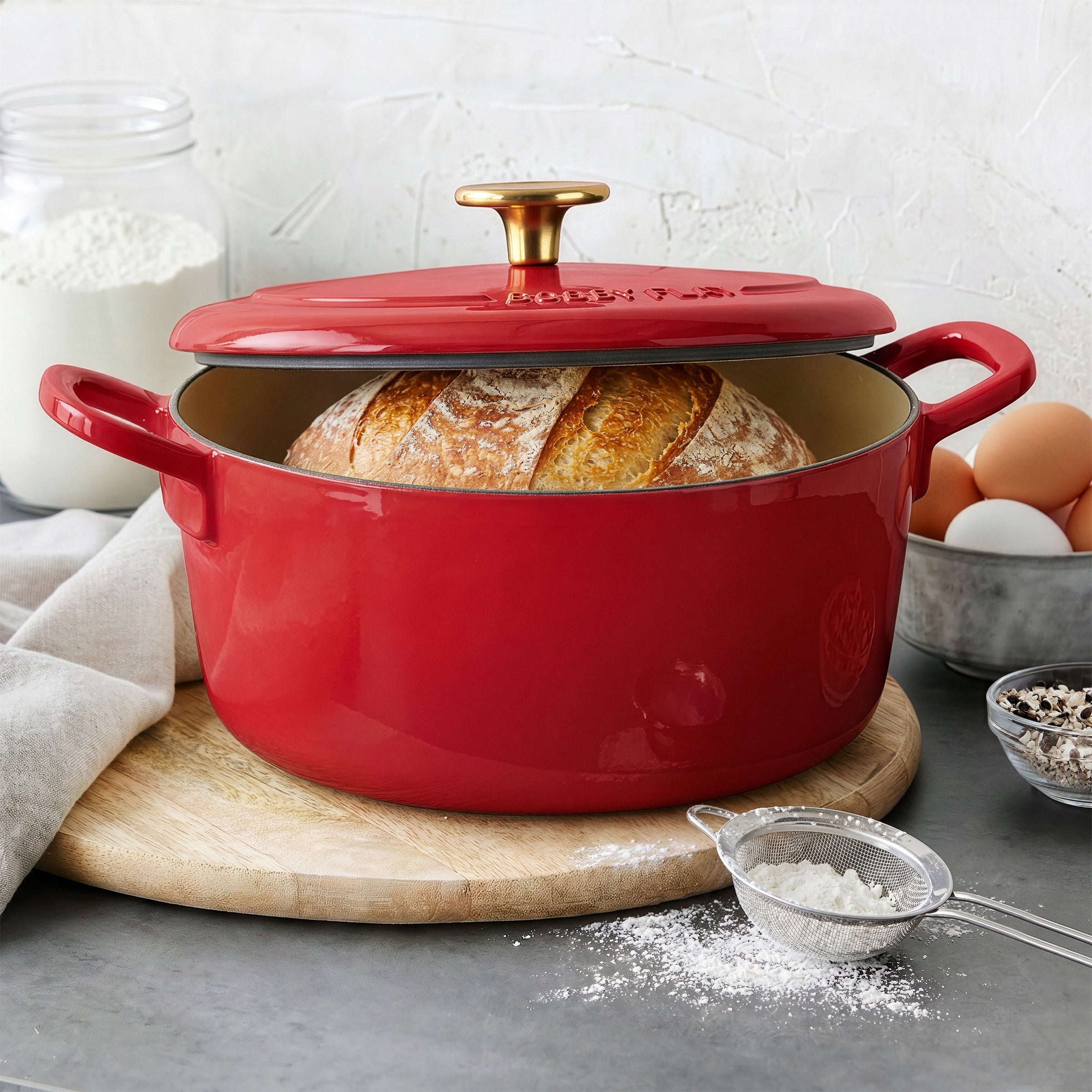 Red Bobby Flay by GreenPan 5.5-quart Dutch oven with a round loaf of bread inside, shown on a kitchen surface.