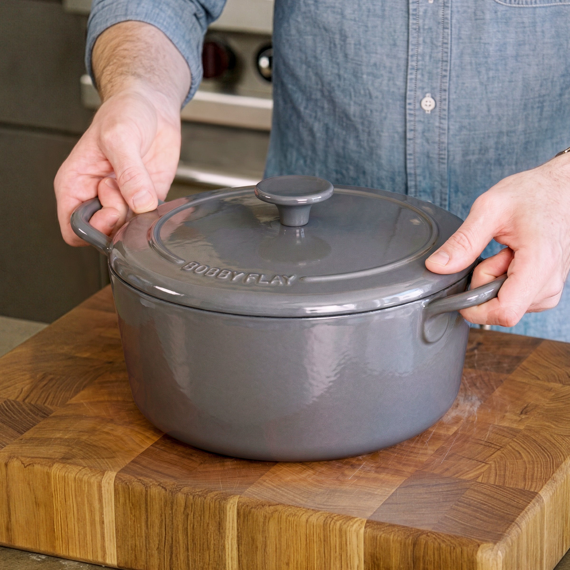 Slate enameled cast iron Dutch oven set by GreenPan on a wooden cutting board in a kitchen, person holding the lid.