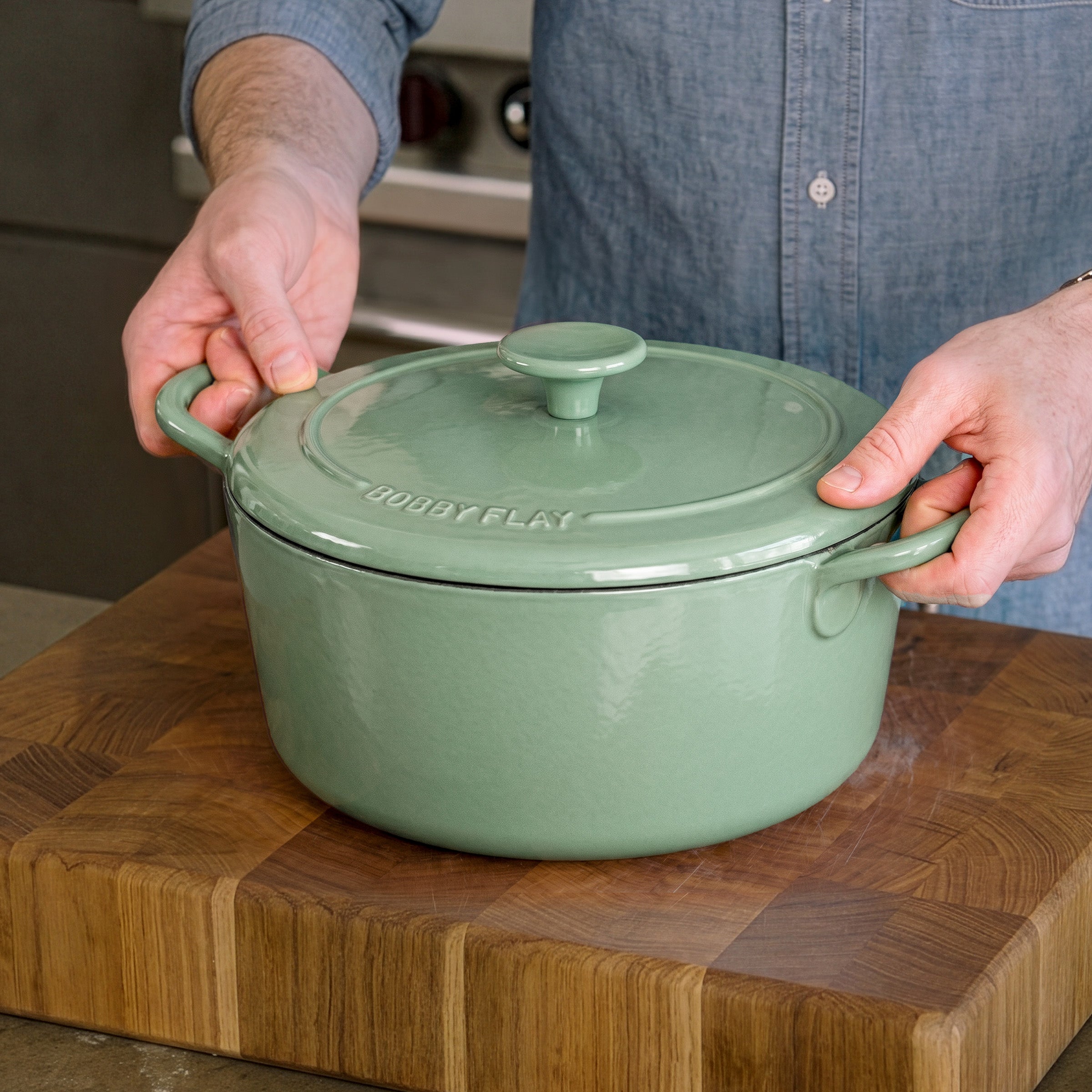 Person holding a sage green enameled cast iron Dutch oven set by GreenPan, 5.5-quart size.