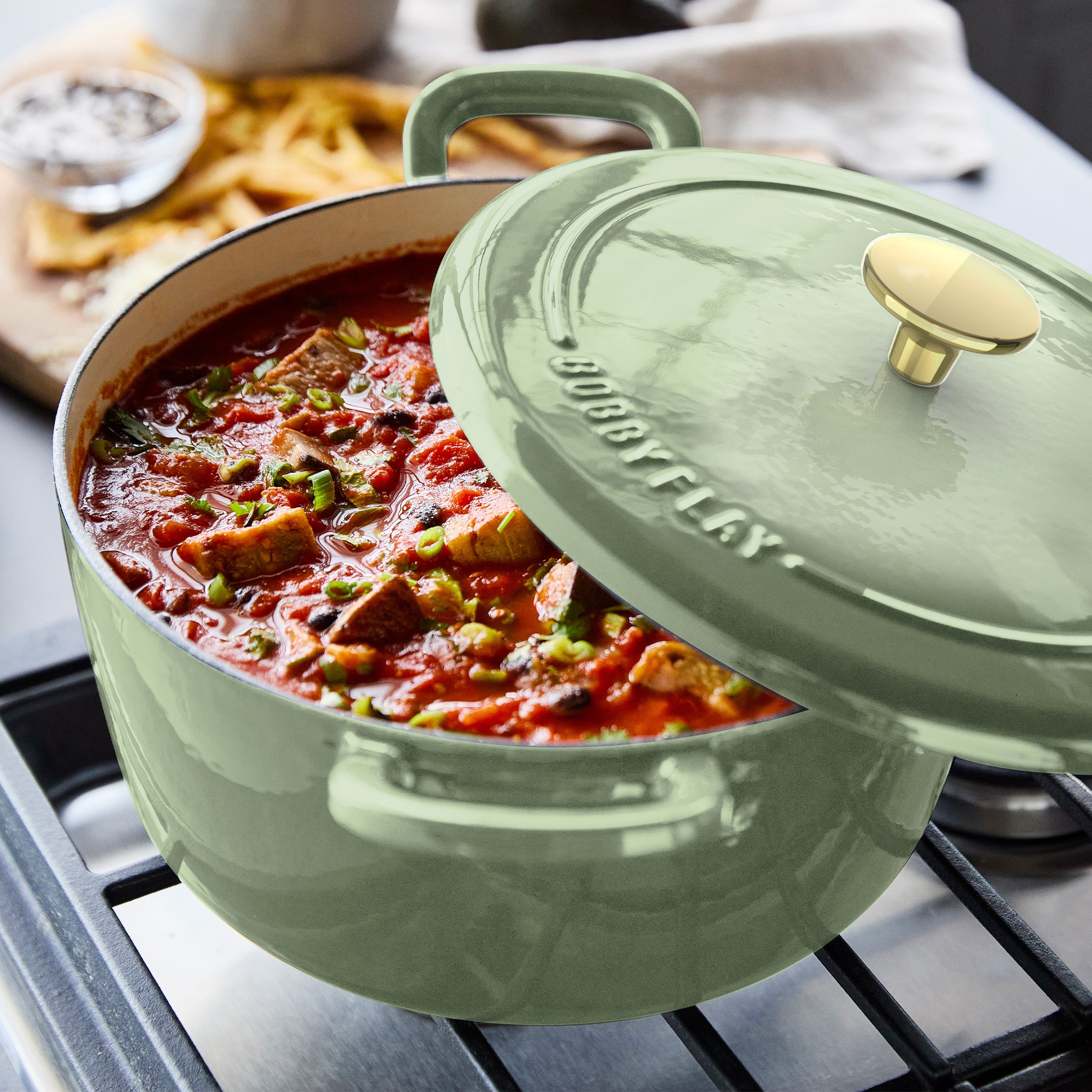Sage green Dutch oven with lid, simmering tomato stew and vegetables. Set includes 3 pieces.