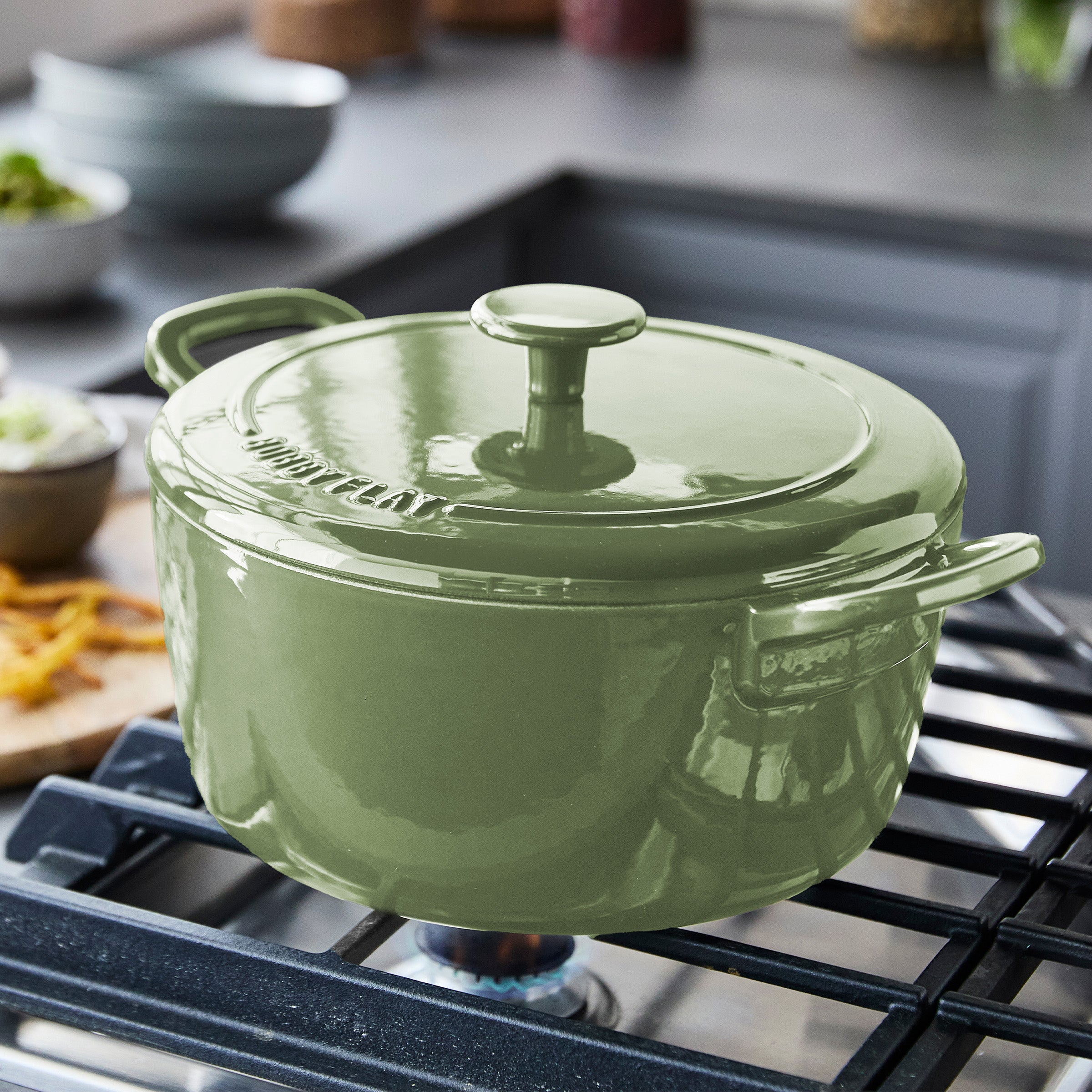Sage green Dutch oven with handles on a stovetop in a modern kitchen.