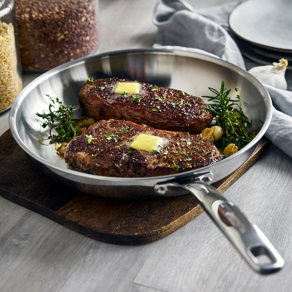 Two seared steaks topped with butter, herbs, and garlic in a 12-inch Chatham Pro stainless steel frypan.