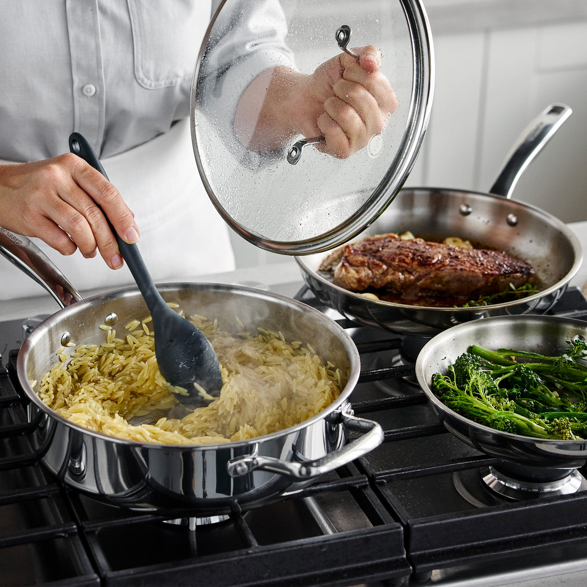 Hands stir orzo, steak, and broccolini in a Chatham Pro stainless steel 12-piece cookware set.