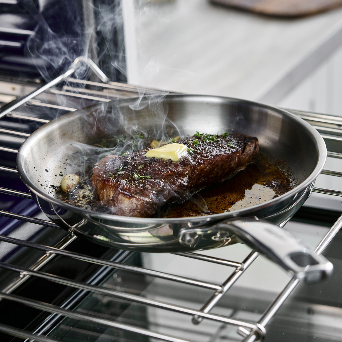 Chatham Pro stainless steel skillet containing a seared steak topped with butter and herbs on an oven rack.