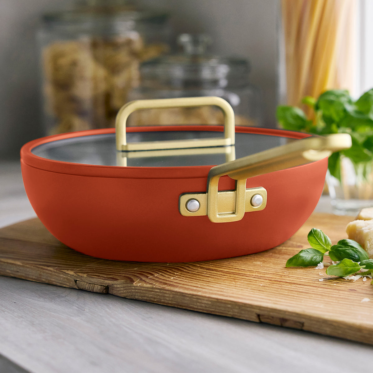 Stanley Tucci 3.25-quart ceramic nonstick Piccolo pan in Amalfi Sunset with gold handle and glass lid on a wooden cutting board.