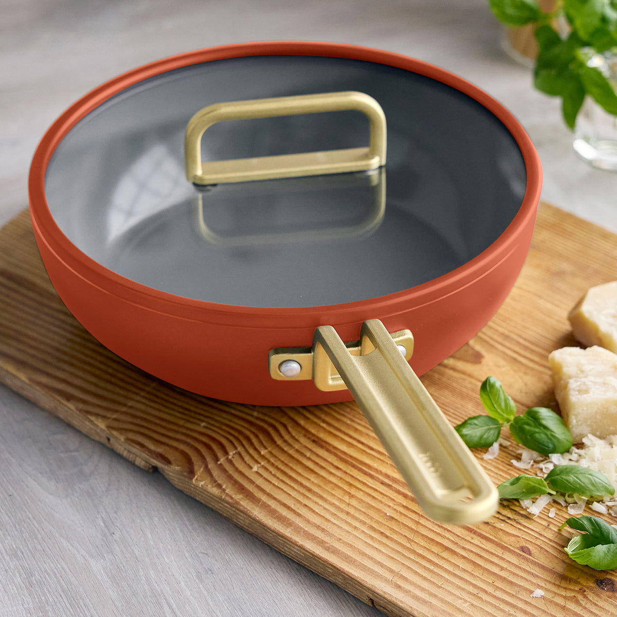 Stanley Tucci 3.25-quart ceramic nonstick Piccolo pan in Amalfi Sunset with a glass lid, displayed on a wooden board with cheese and basil.