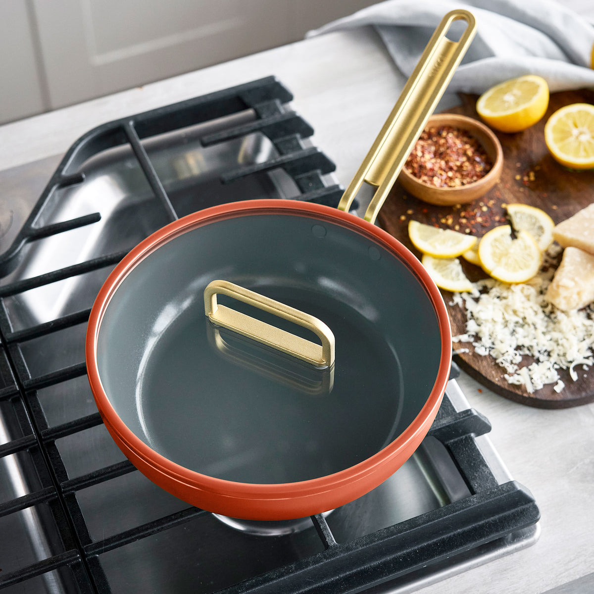 Stanley Tucci 3.25-quart ceramic nonstick Piccolo pan in Amalfi Sunset with a grey interior and gold-toned lid, shown cooking on a stovetop.
