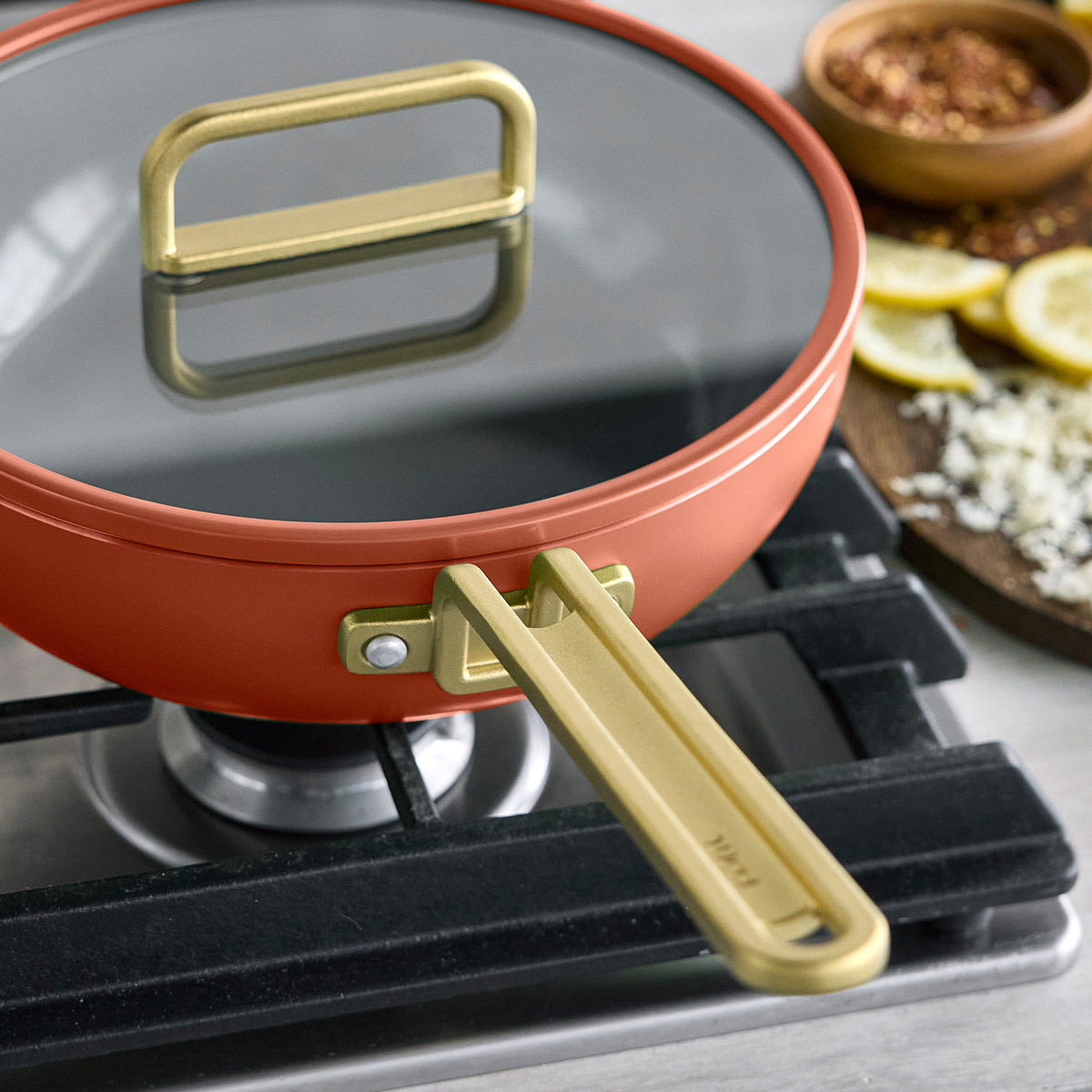Stanley Tucci 3.25-quart ceramic nonstick Piccolo pan in Amalfi Sunset with matching lid and gold-tone handles on a stovetop.