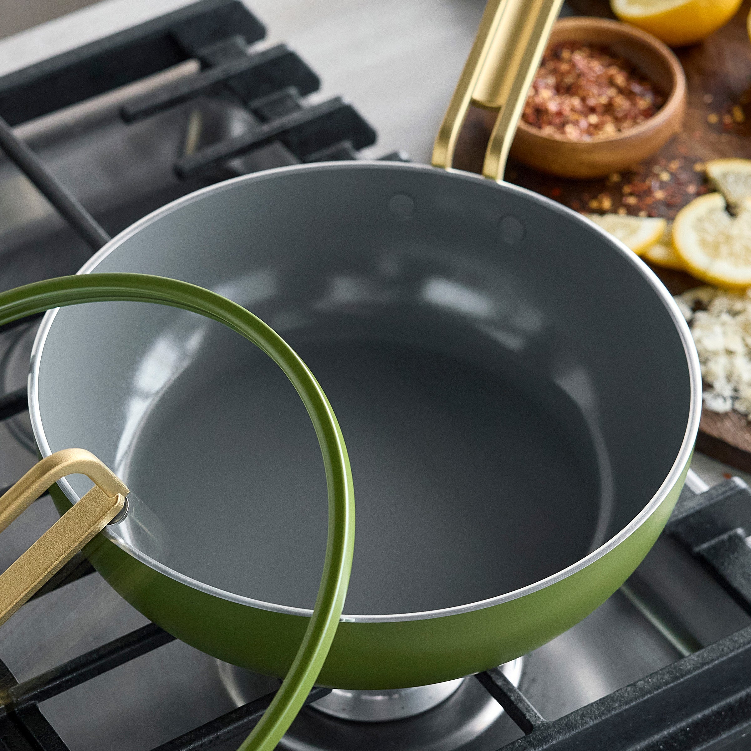 Green ceramic nonstick piccolo pan with lid, lemons and spices beside it.