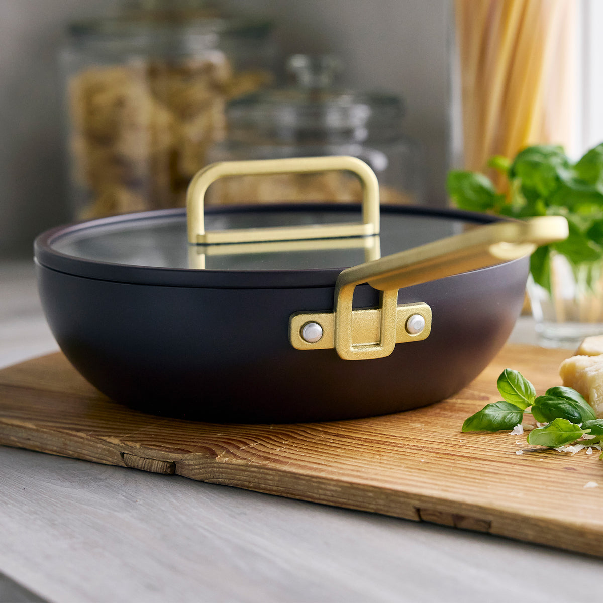 Stanley Tucci 3.25-quart espresso ceramic nonstick Piccolo pan with glass lid and gold-tone handles on a wooden cutting board.