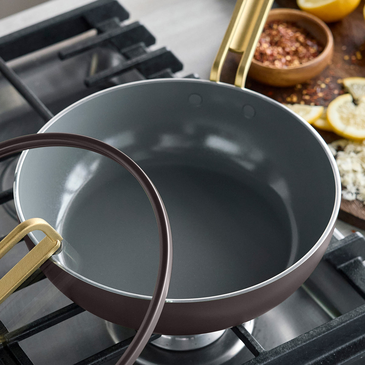 Stanley Tucci 3.25-quart espresso ceramic piccolo pan with a gold handle and glass lid on a stovetop.