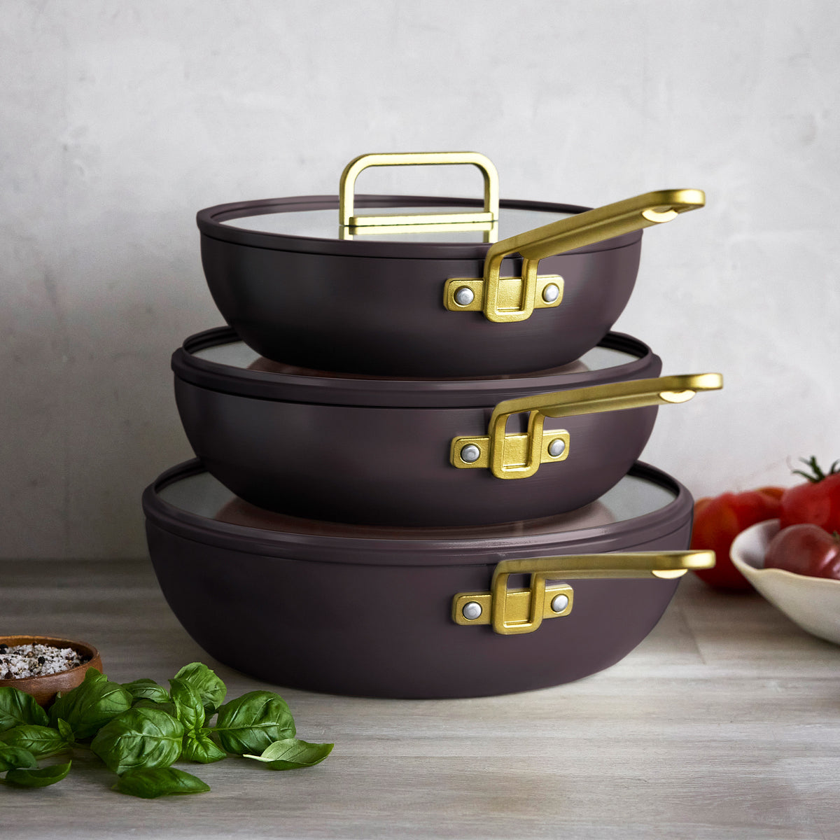 Three 3.25-quart Stanley Tucci ceramic nonstick Piccolo pans in espresso with gold-tone handles stacked on a countertop.