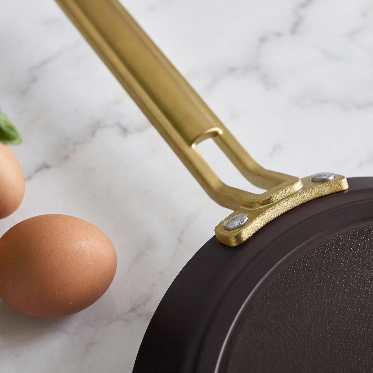Stanley Tucci 10-inch ceramic nonstick crepe and omelette pan in espresso with a gold-tone handle, shown with two eggs.