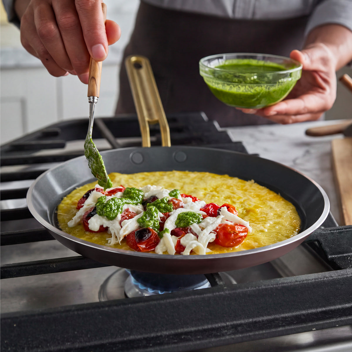 Pesto being drizzled over a tomato and cheese omelette in a 10″ Stanley Tucci Ceramic Nonstick Crepe and Omelette Pan on a stove.