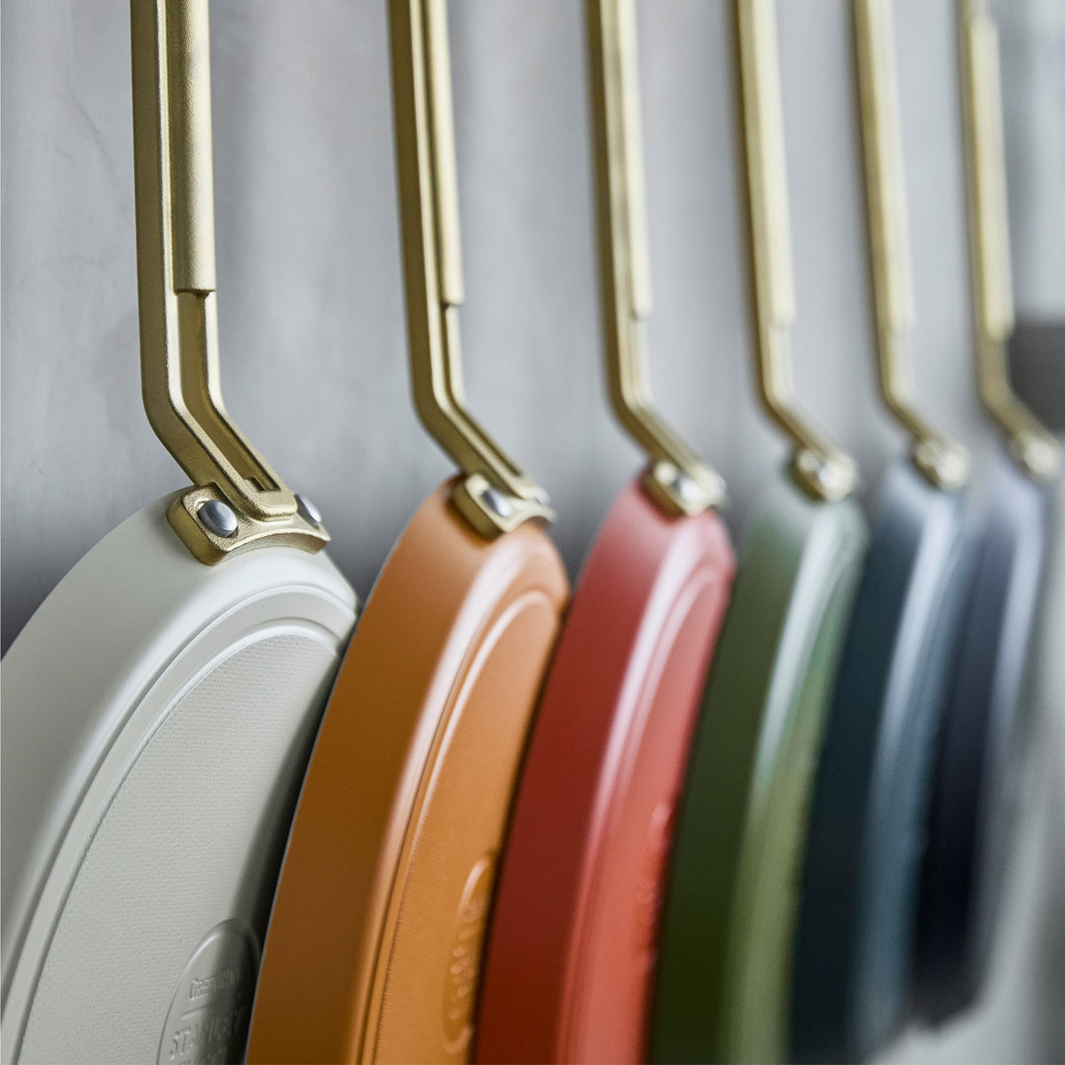 Stanley Tucci ceramic nonstick 10-inch crepe and omelette pans in espresso with metallic handles, hanging in a row on a wall.