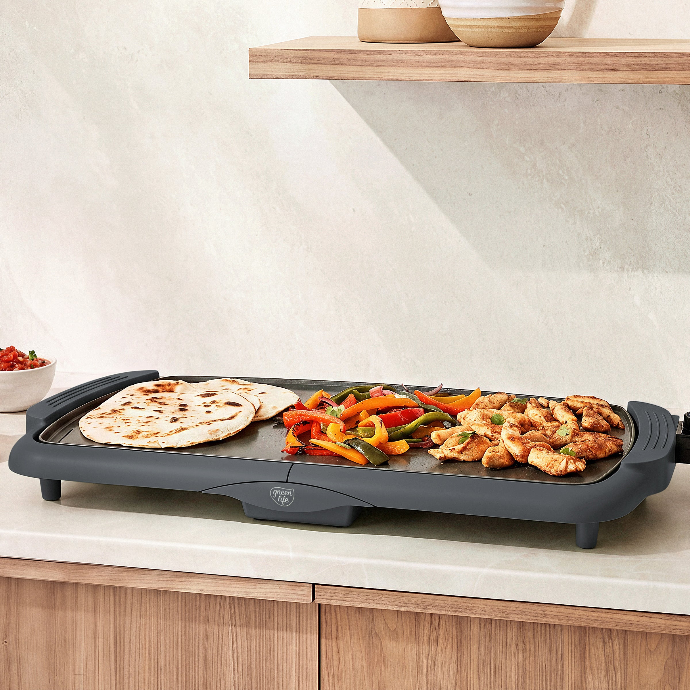 Gray GreenLife electric griddle with tortillas, bell peppers, and chicken cooking on a kitchen counter.
