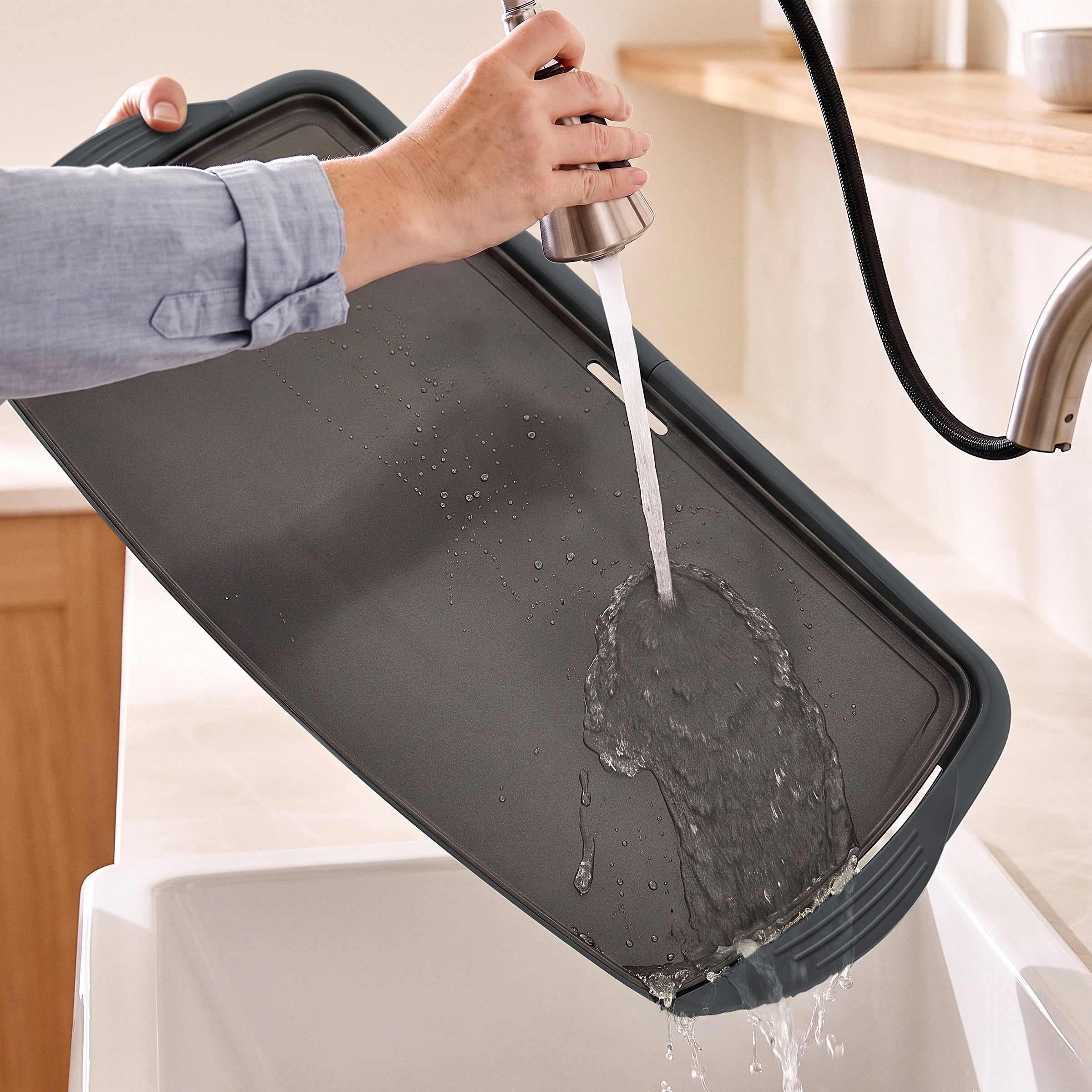 A GreenLife Griddle XL in graphite being rinsed under a kitchen faucet over a white sink.