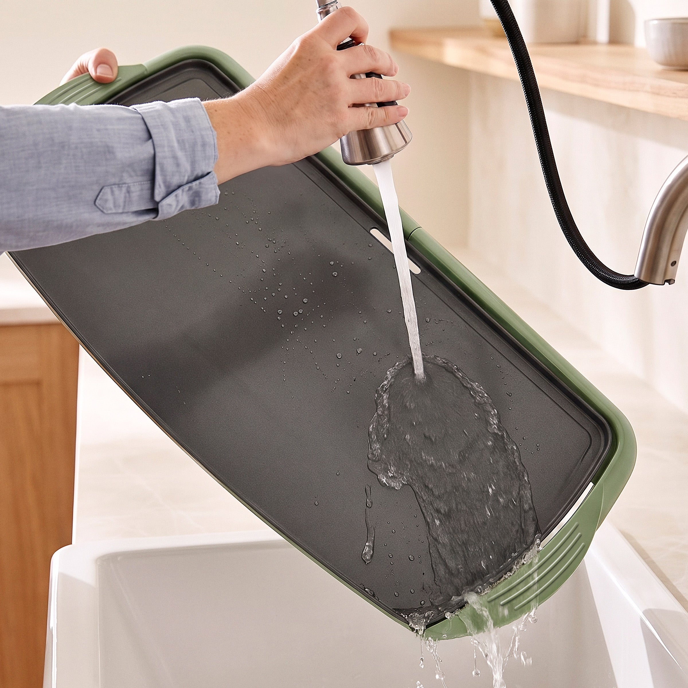 Rinsing a GreenLife Griddle XL in Sage under running faucet, water flowing over the non-stick surface into the sink.