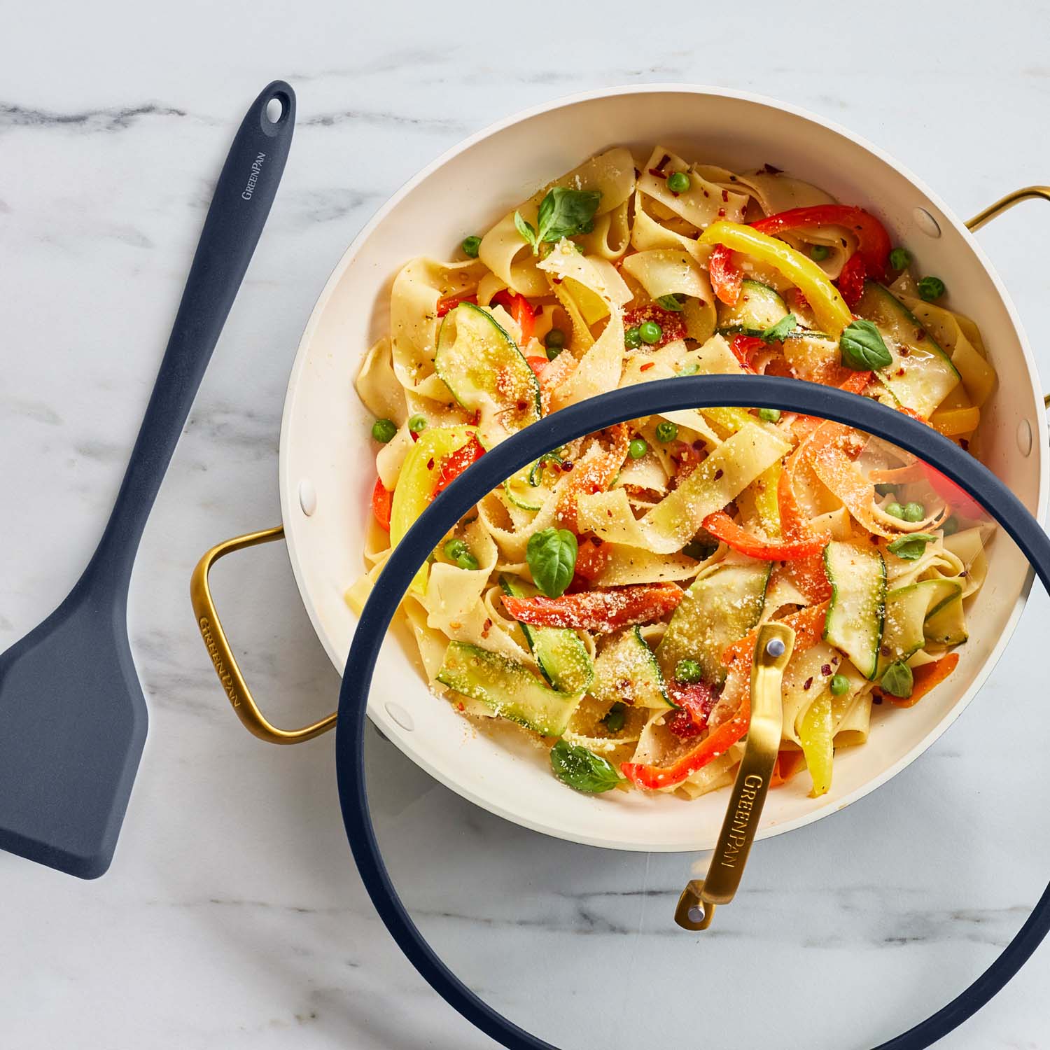 Vegetable ribbon pasta in a twilight blue ceramic nonstick pan with lid on marble, spatula placed beside the pan.