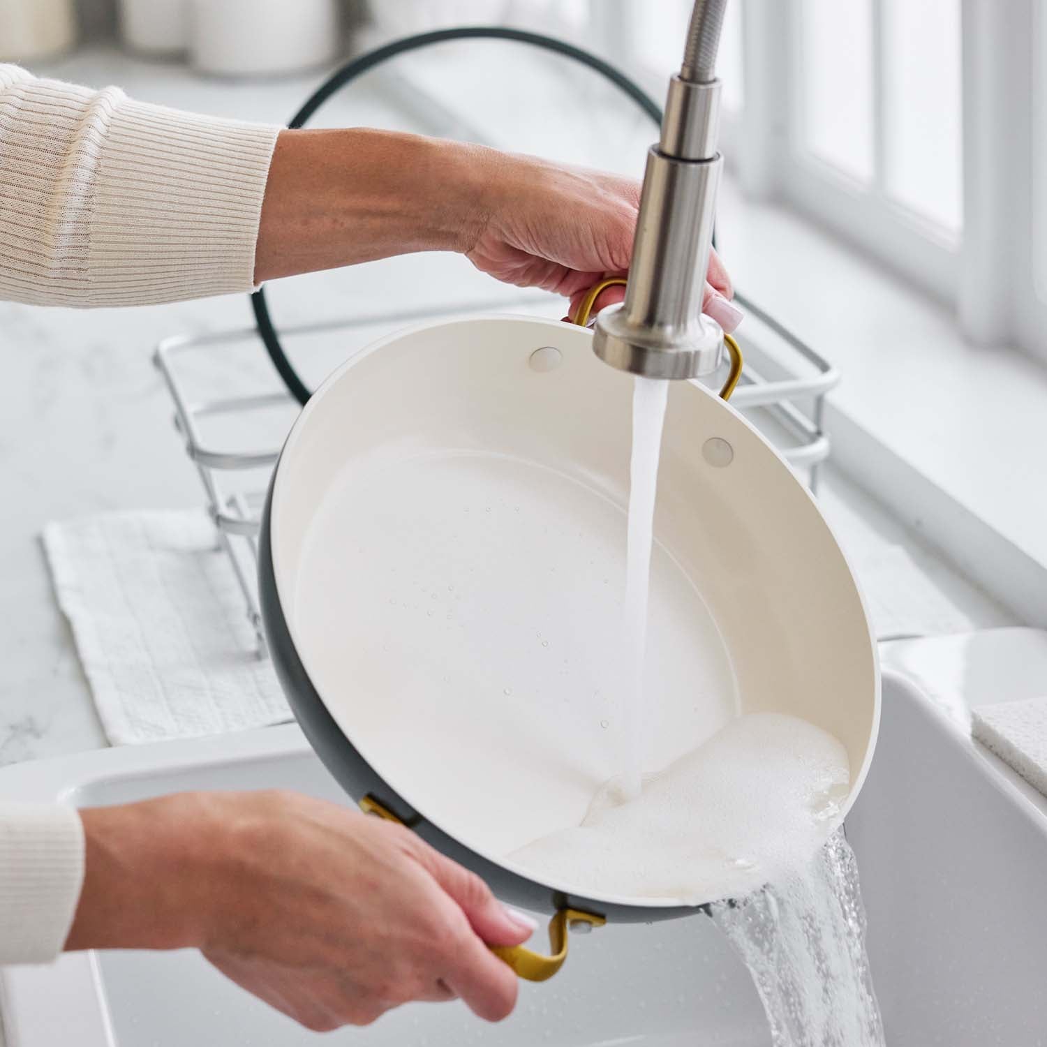 Ceramic nonstick 3.75-quart everyday pan with lid in twilight blue being washed under running water with soap suds.