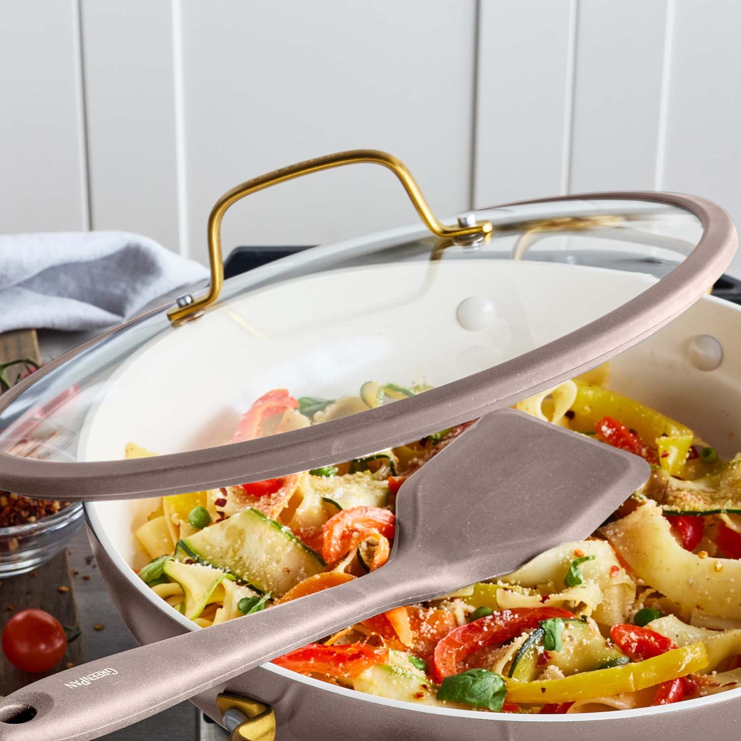 Ceramic nonstick 3.75-qt pan with glass lid holding pasta and vegetables; spatula rests on the skillet.