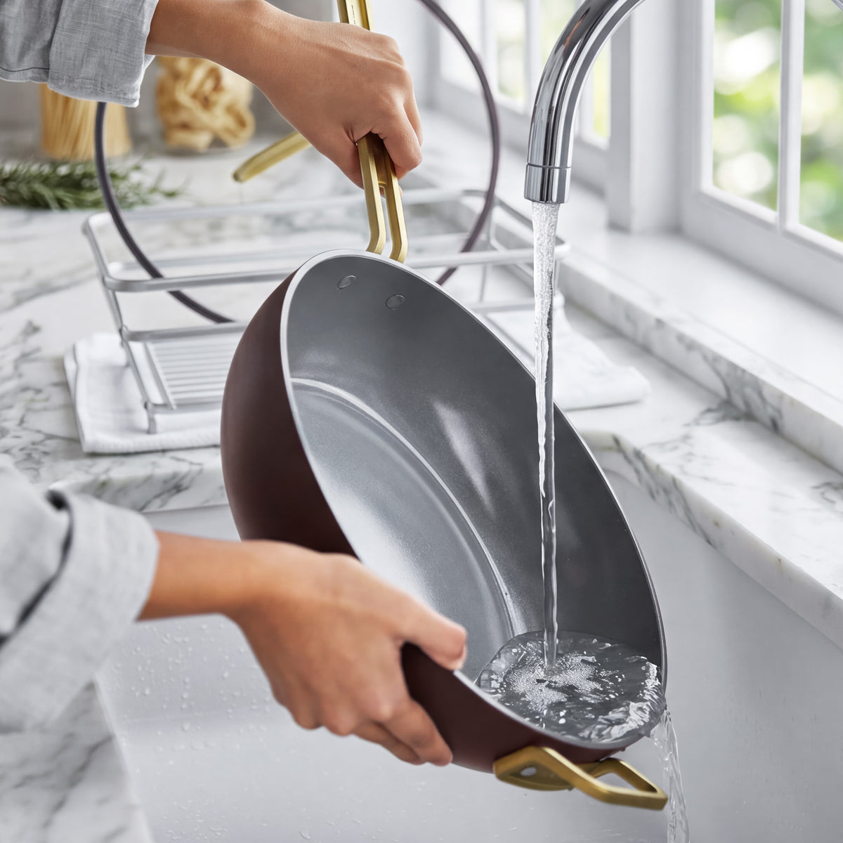 Espresso Stanley Tucci™ ceramic nonstick 6.5-quart essential pan with gold-tone handles being rinsed under a kitchen faucet.
