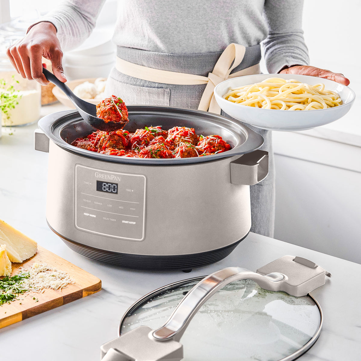 Person serving meatballs from an 8-quart slow cooker, holding a bowl of spaghetti in the other hand.