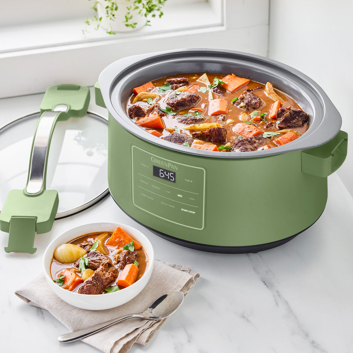 Sage 8-quart slow cooker filled with beef stew, next to a bowl of stew on a white surface.