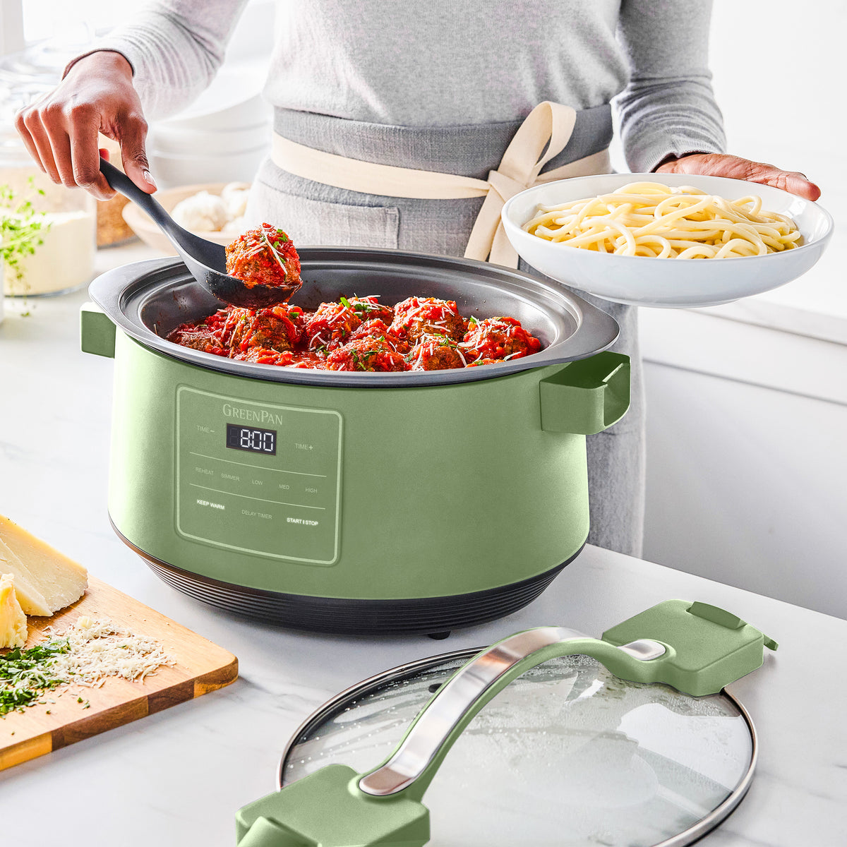 Sage 8-quart slow cooker with locking lid on kitchen counter, serving meatballs; person holding spaghetti nearby.