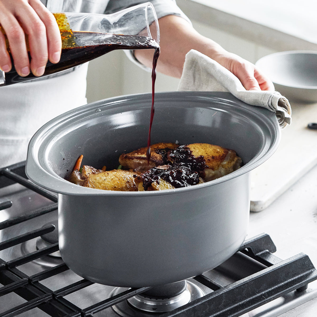 Red wine being poured over chicken inside an 8-quart sage green slow cooker with a locking lid on a stovetop.