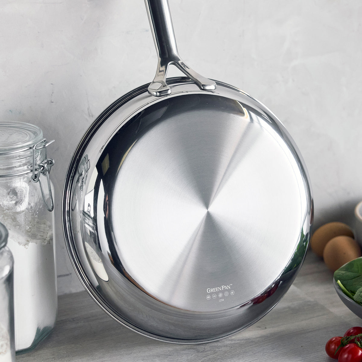 Gray ceramic nonstick 10-inch frypan hanging on a gray wall above a kitchen counter with food and jars.