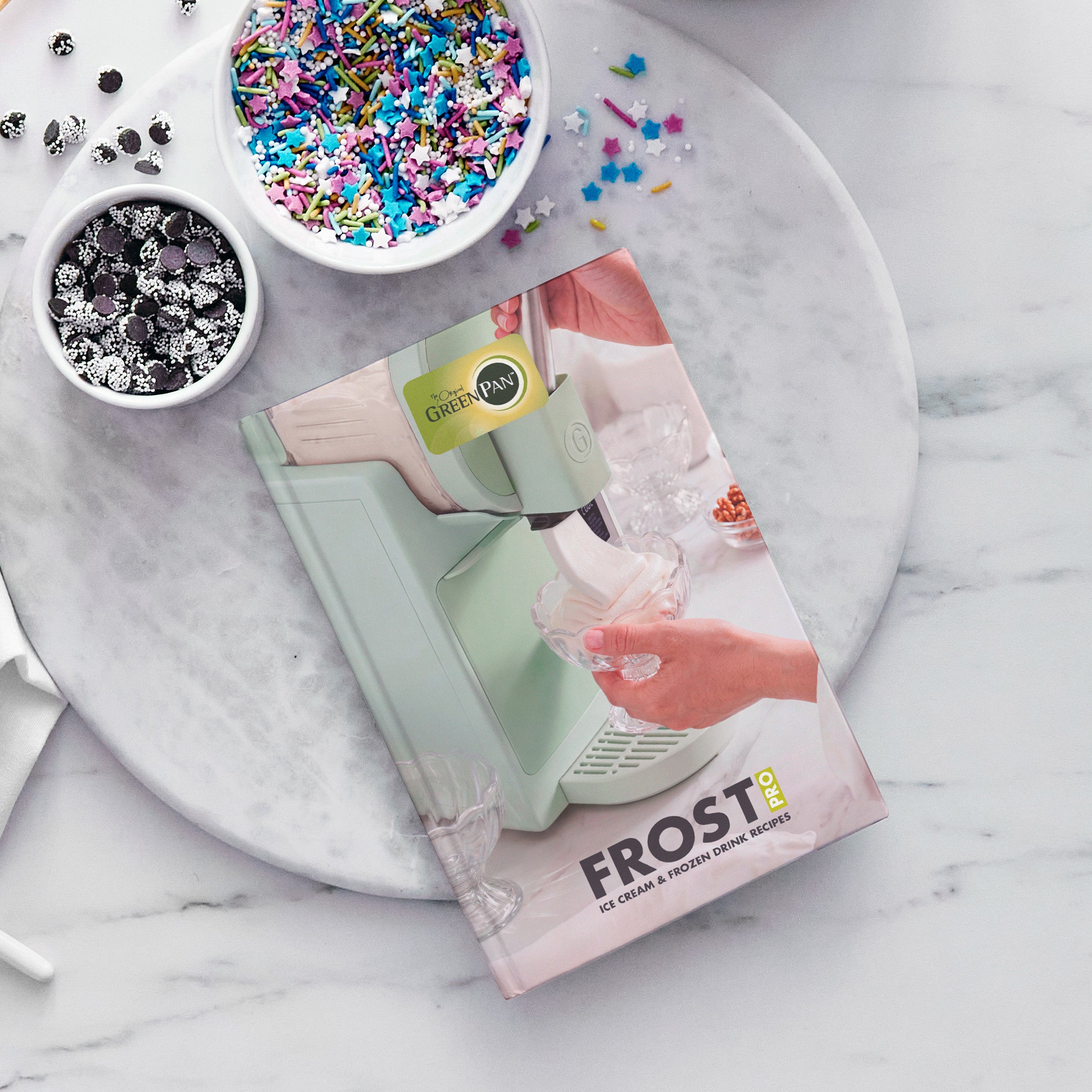 Ice cream and frozen drink recipe book on a marble surface with colorful sprinkles and candies around it.