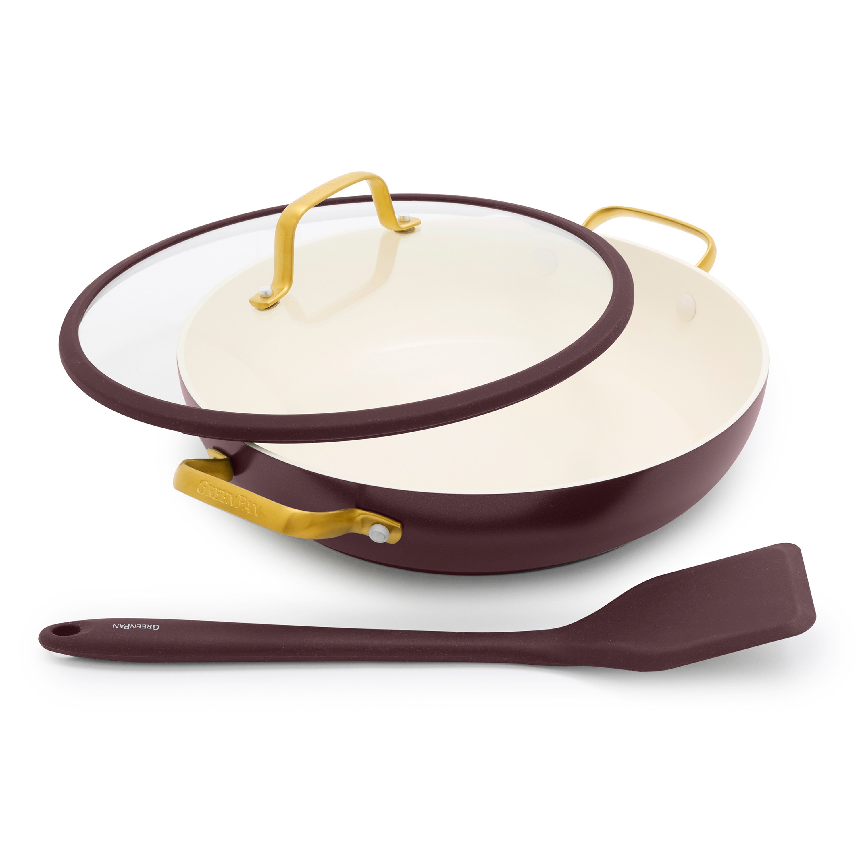 Maroon everyday pan with gold handles, glass lid, and matching spatula in front.