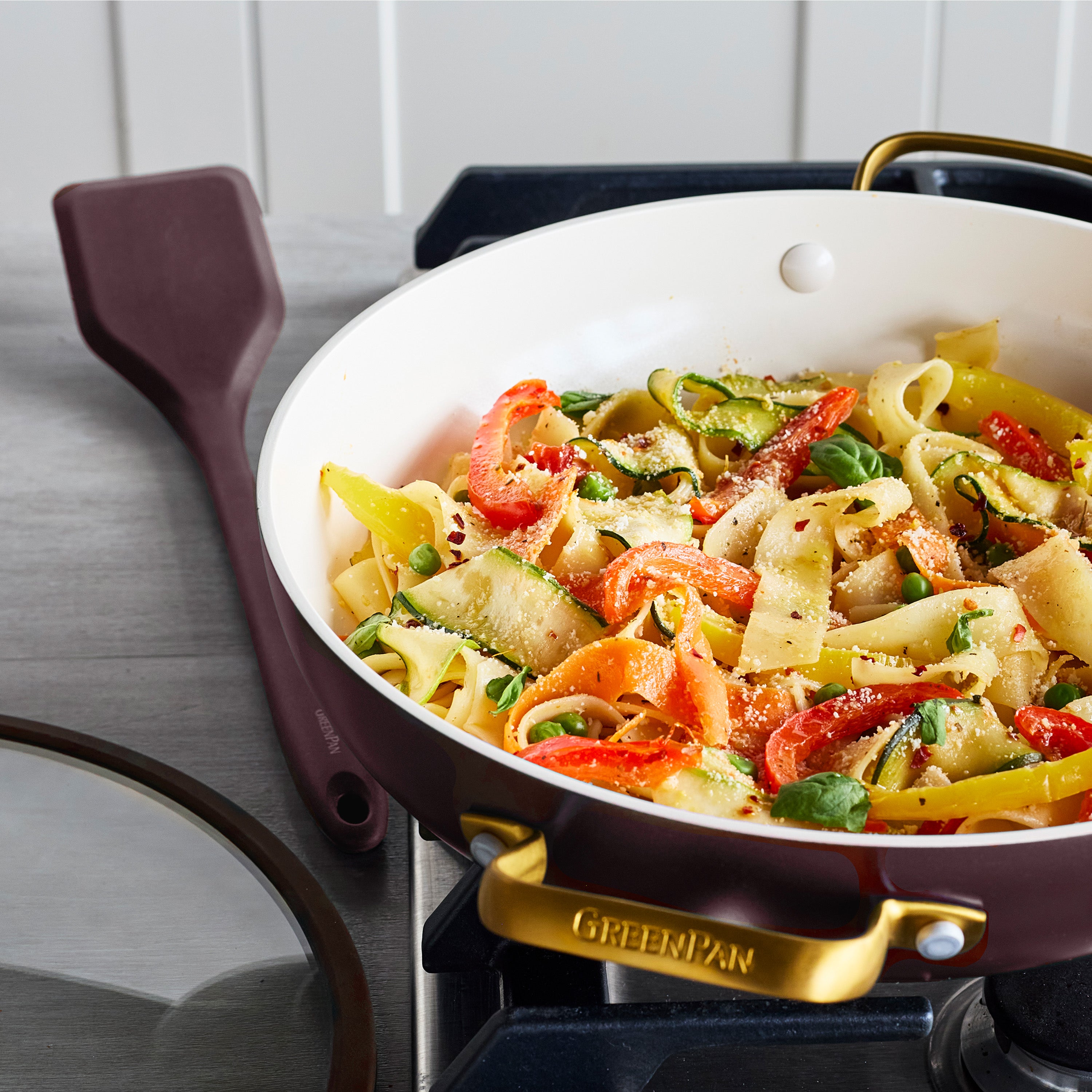Bordeaux ceramic nonstick everyday pan with lid and spatula on stove, filled with veggie pasta.