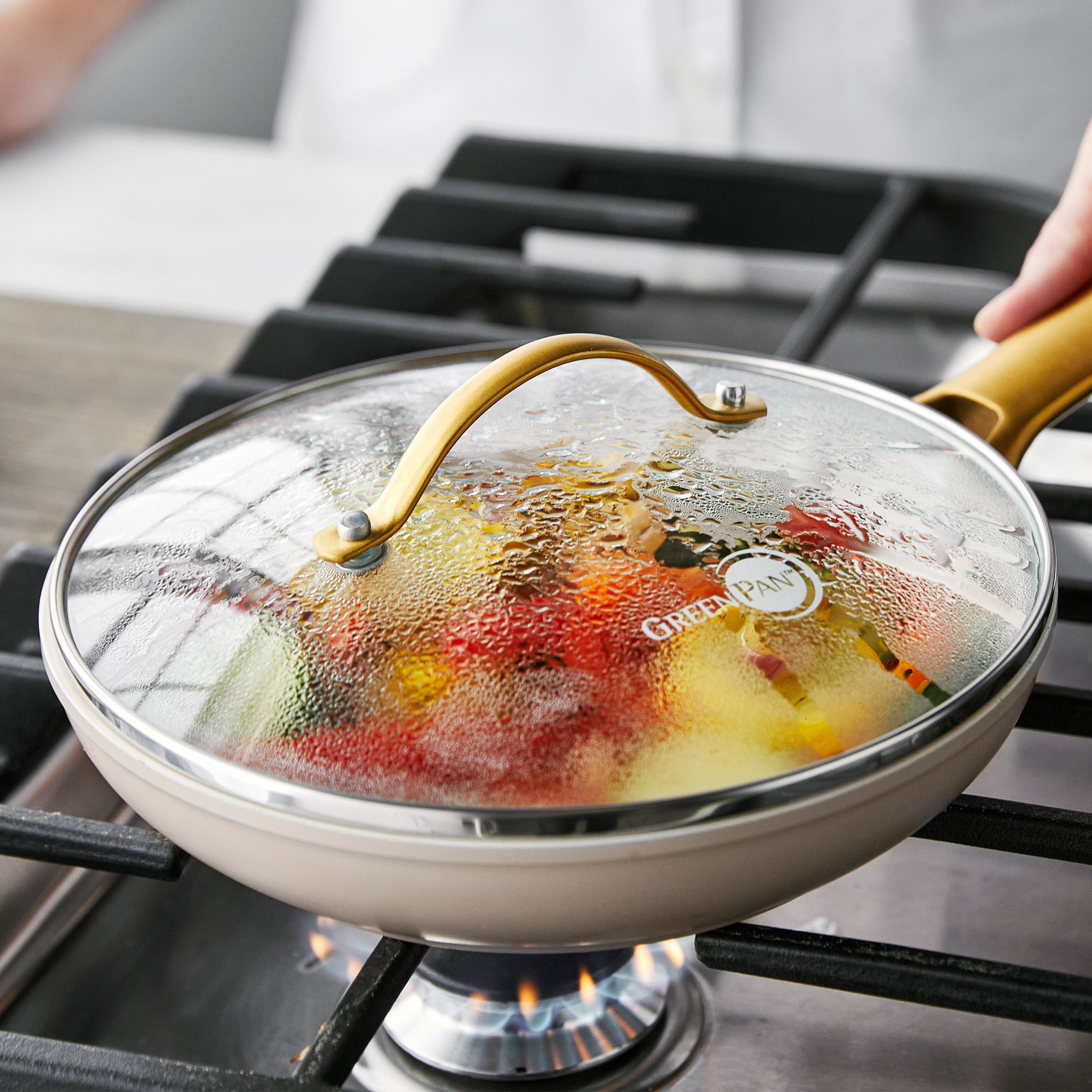 Set of two glass pan lids with stainless steel handles covering pans on a gas stove, visible steam under the lids.