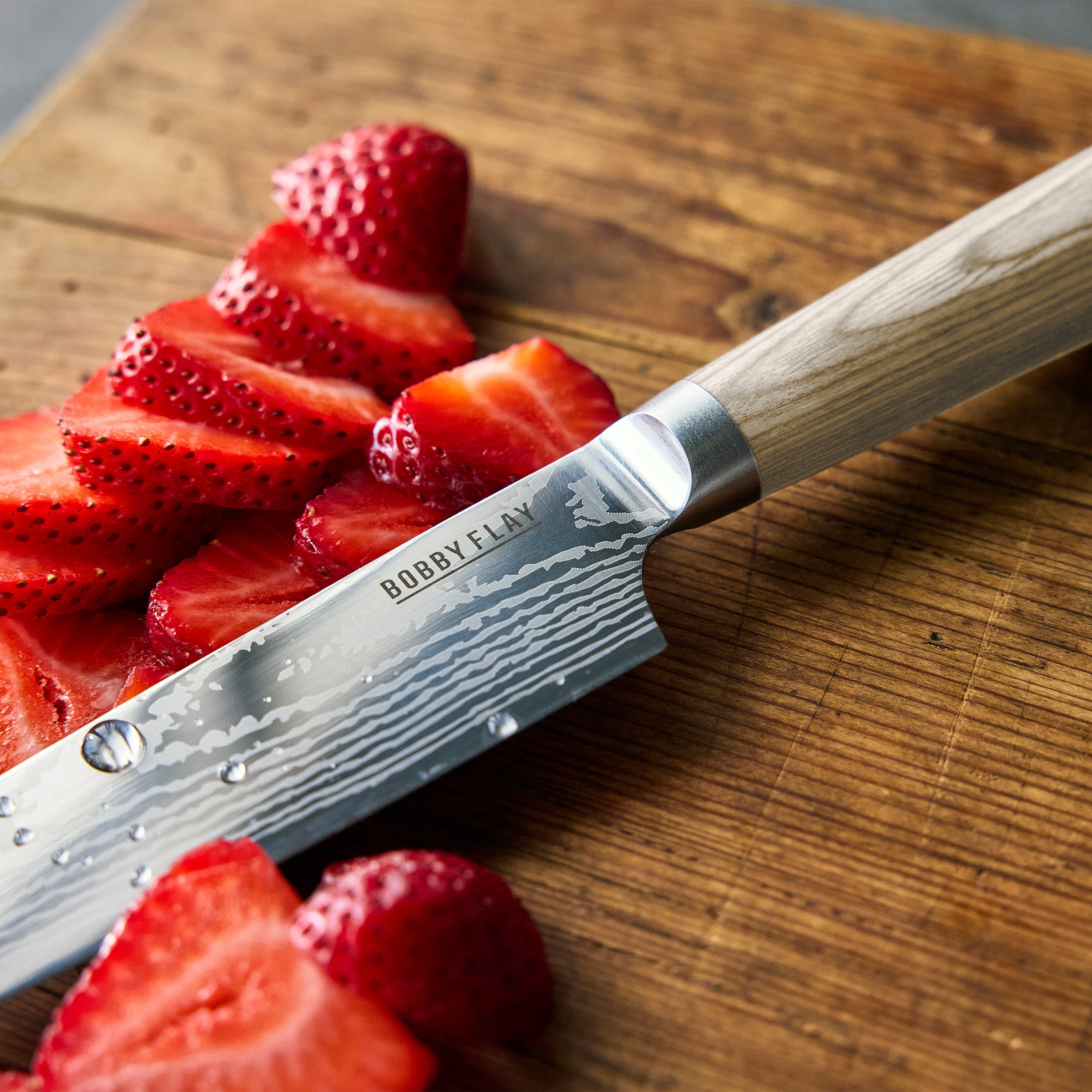 Bobby Flay knife on a wooden cutting board with sliced strawberries