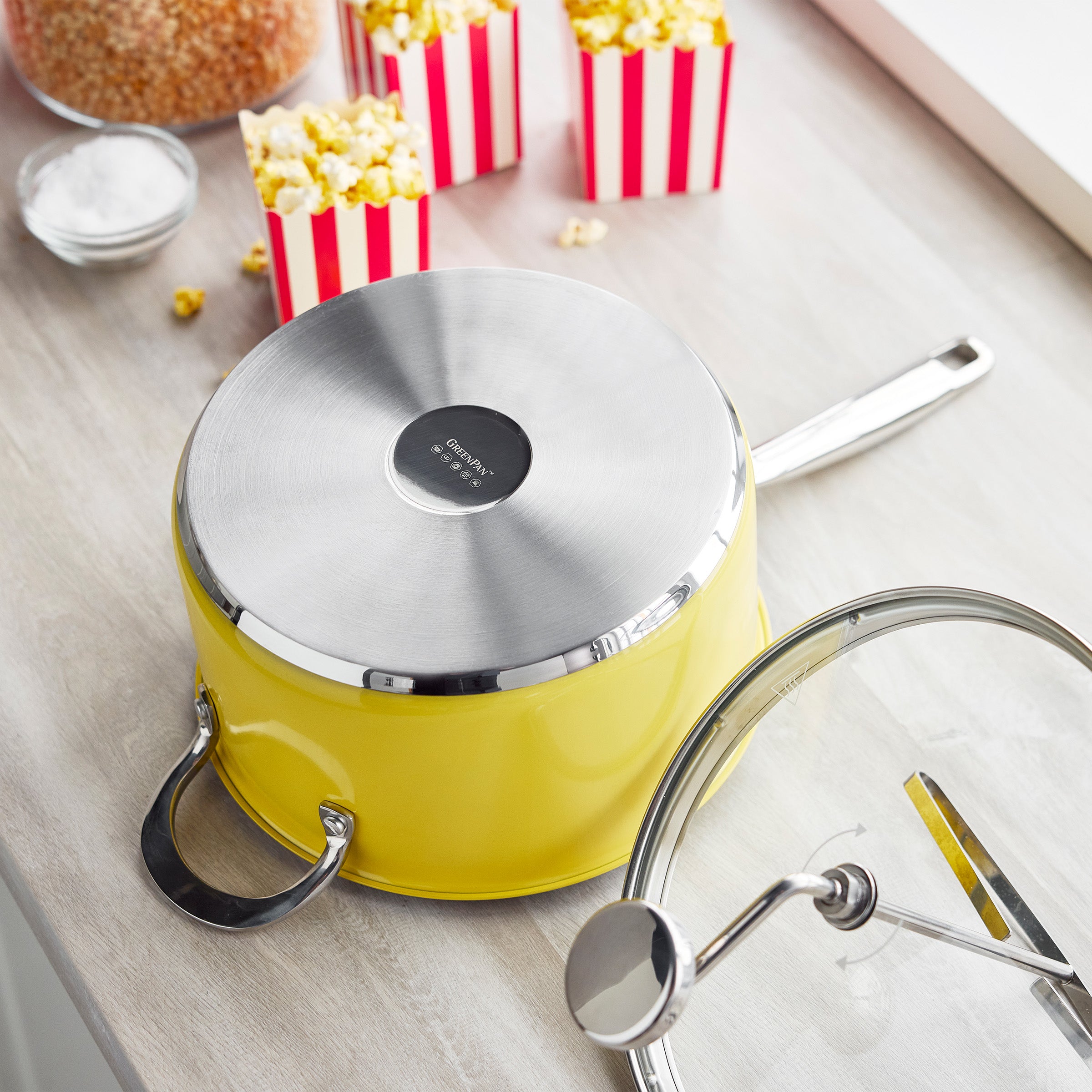 Yellow popcorn maker on a kitchen counter with two bowls of popcorn and a small dish of salt nearby.
