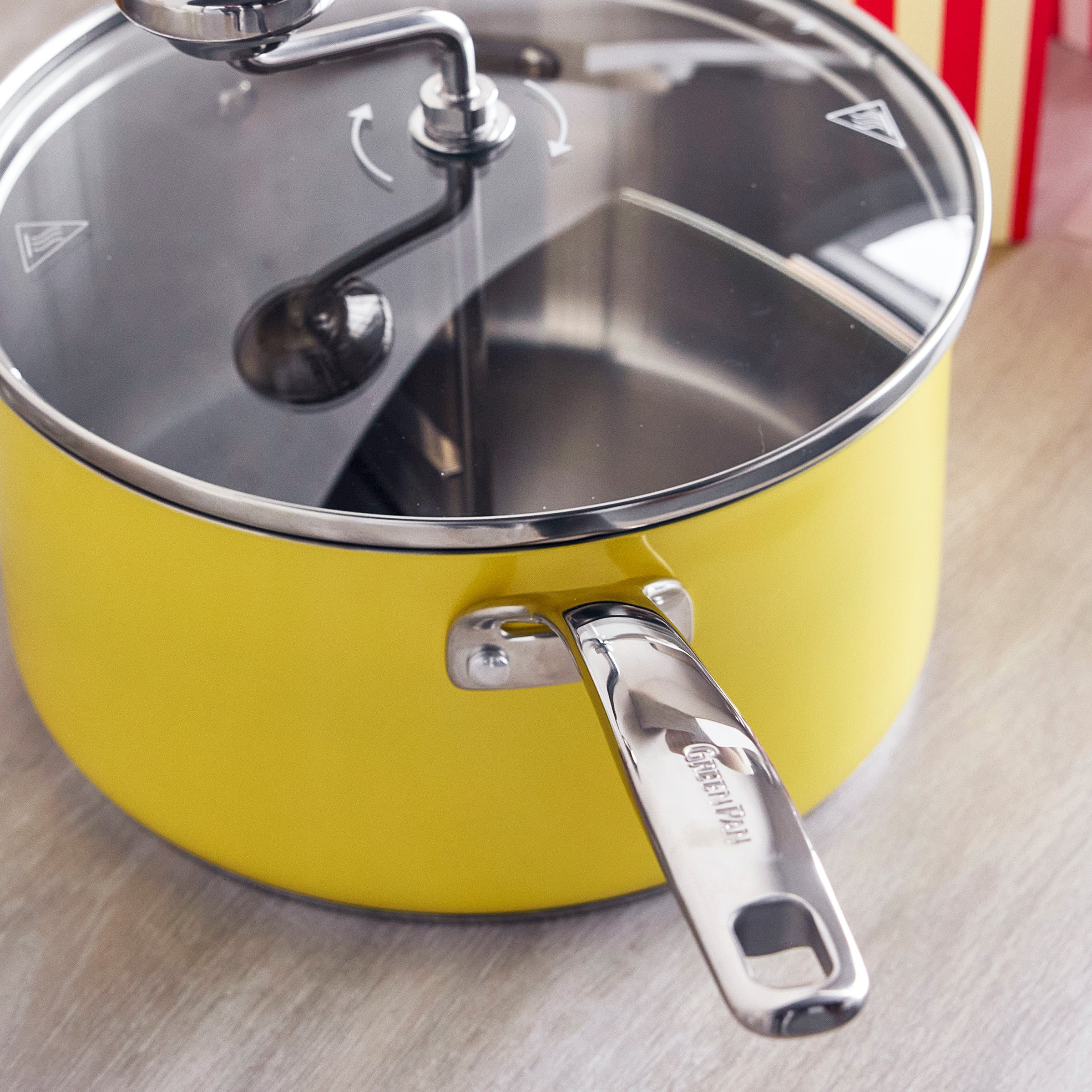 Yellow popcorn maker with glass lid, stainless steel handle, and built-in stirrer on a light countertop.