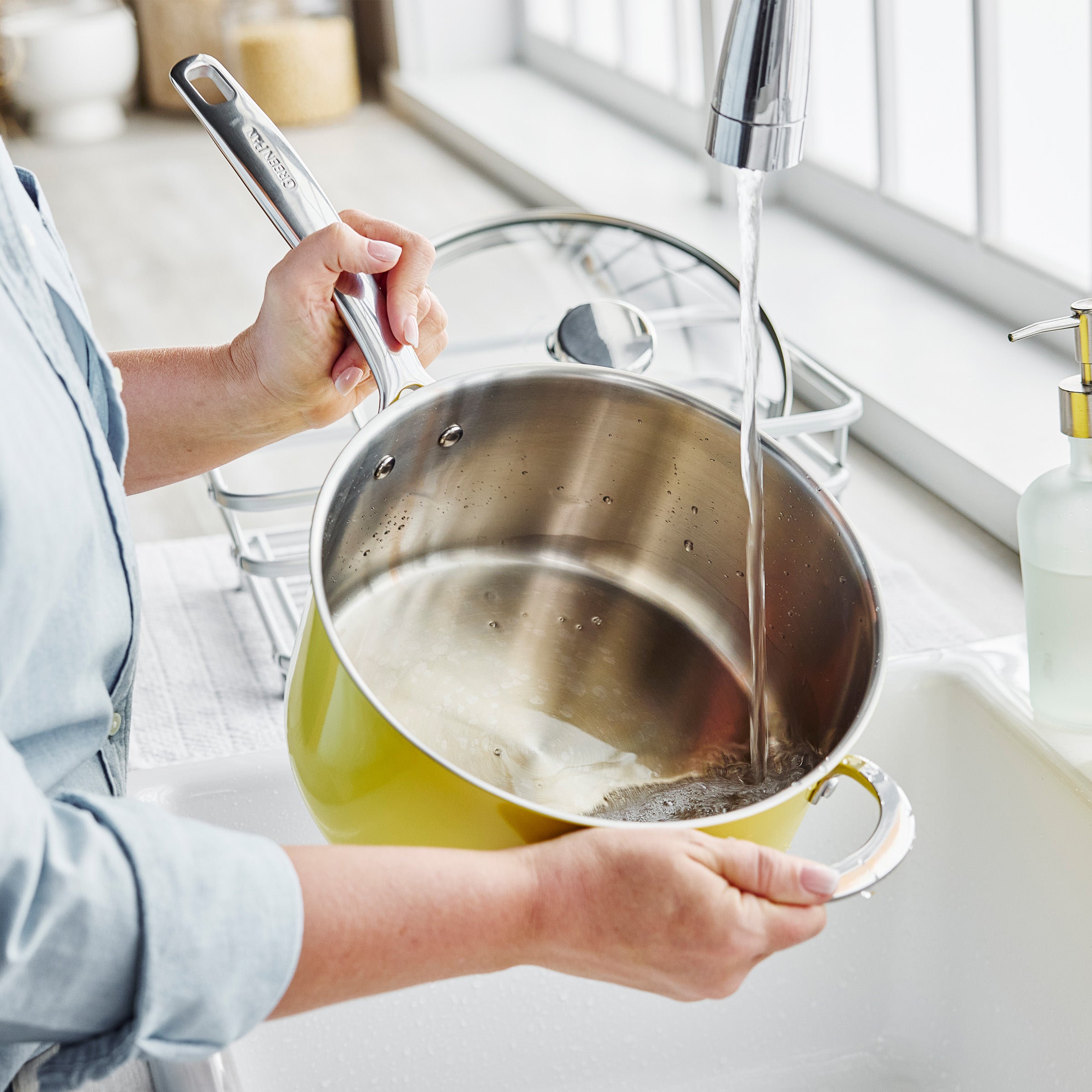 Yellow Big Popper Popcorn Maker being washed with soap and water in a kitchen sink, visible suds inside.