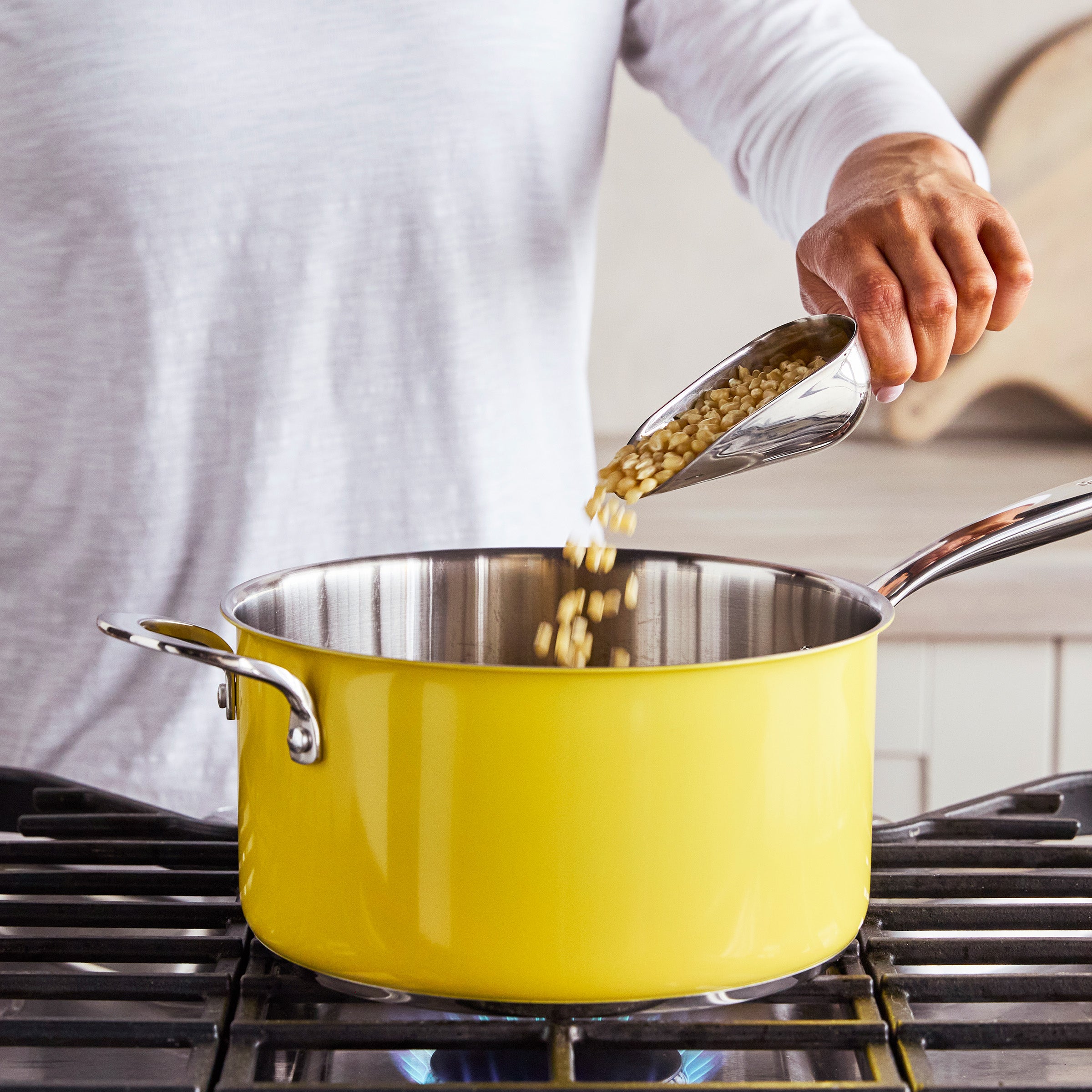 Grains being poured from a scoop into a yellow popcorn maker on a stovetop.