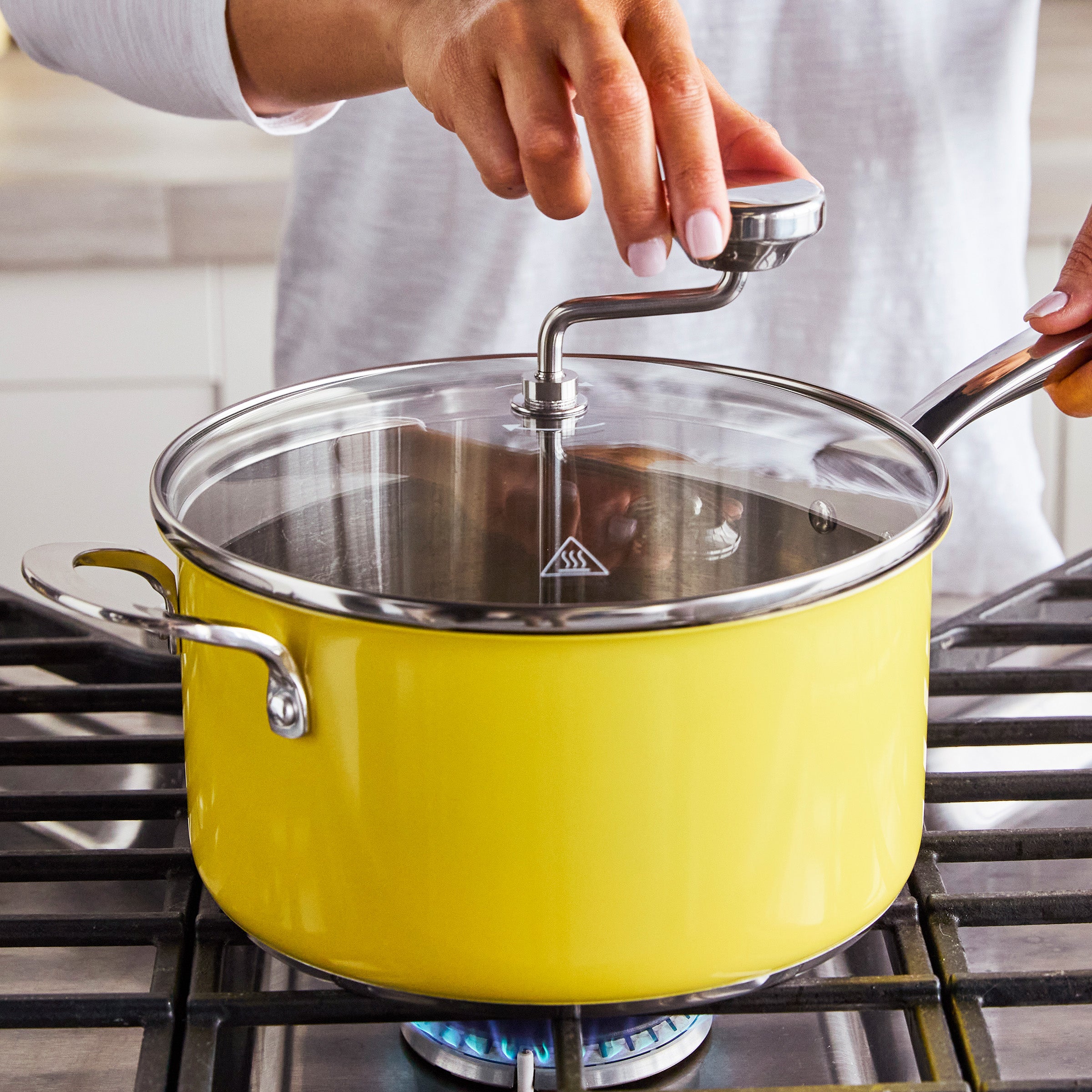 Person turning the handle of a yellow stovetop popcorn maker while it heats on a burner.