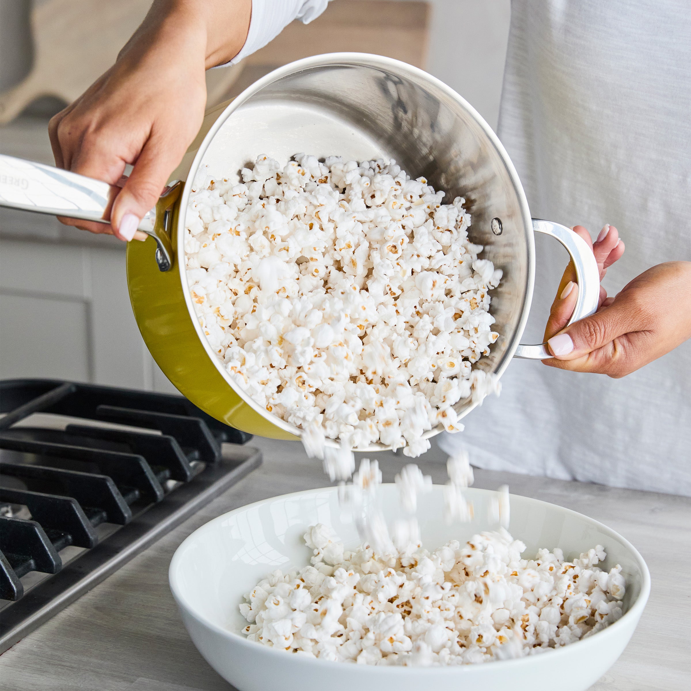Yellow Big Popper Popcorn Maker pouring popcorn into a white bowl on a kitchen counter.