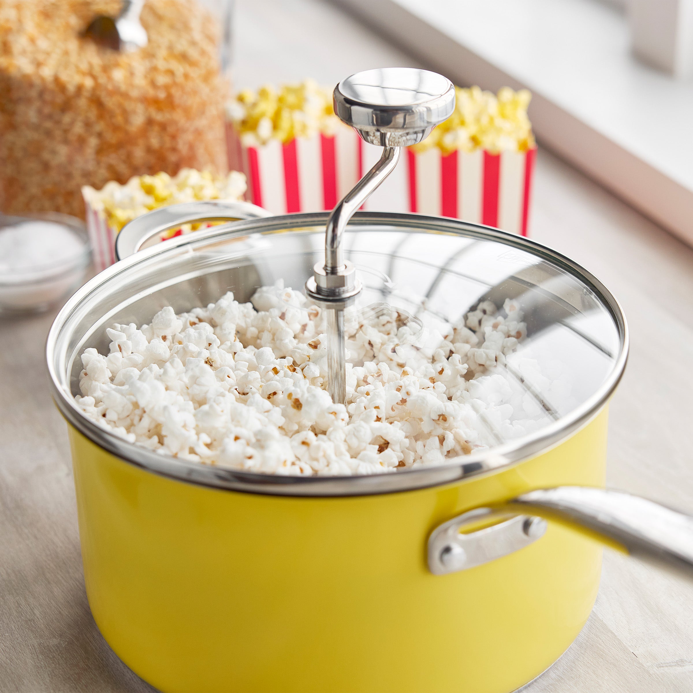 Yellow popcorn maker with fresh popcorn in red-striped containers on a light wood surface.