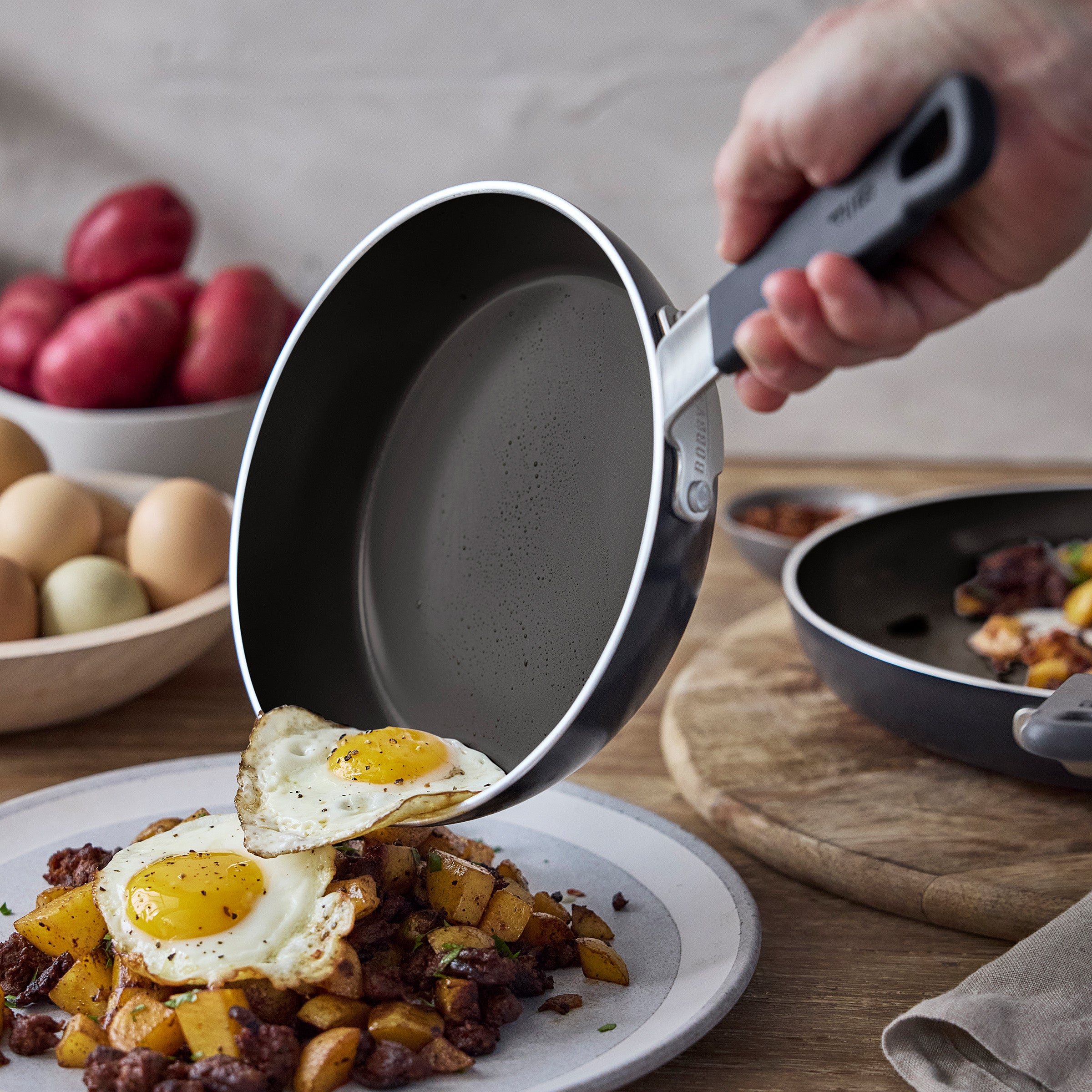 Serving sunny-side-up eggs from a GreenPan ceramic nonstick pan onto potatoes and meat.