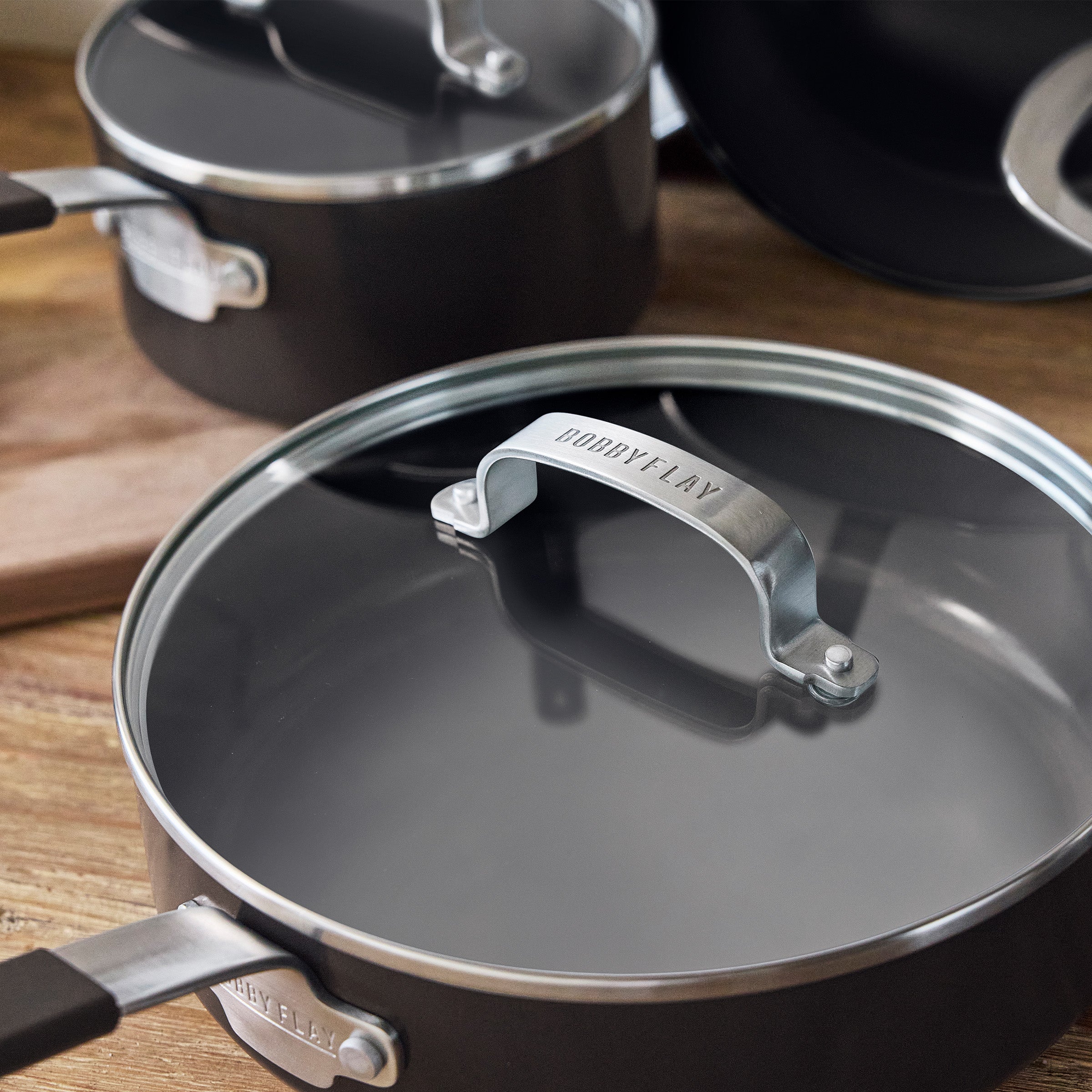 Black saucepan with metal handle from the Bobby Flay by GreenPan 10-piece cookware set on a wooden surface.