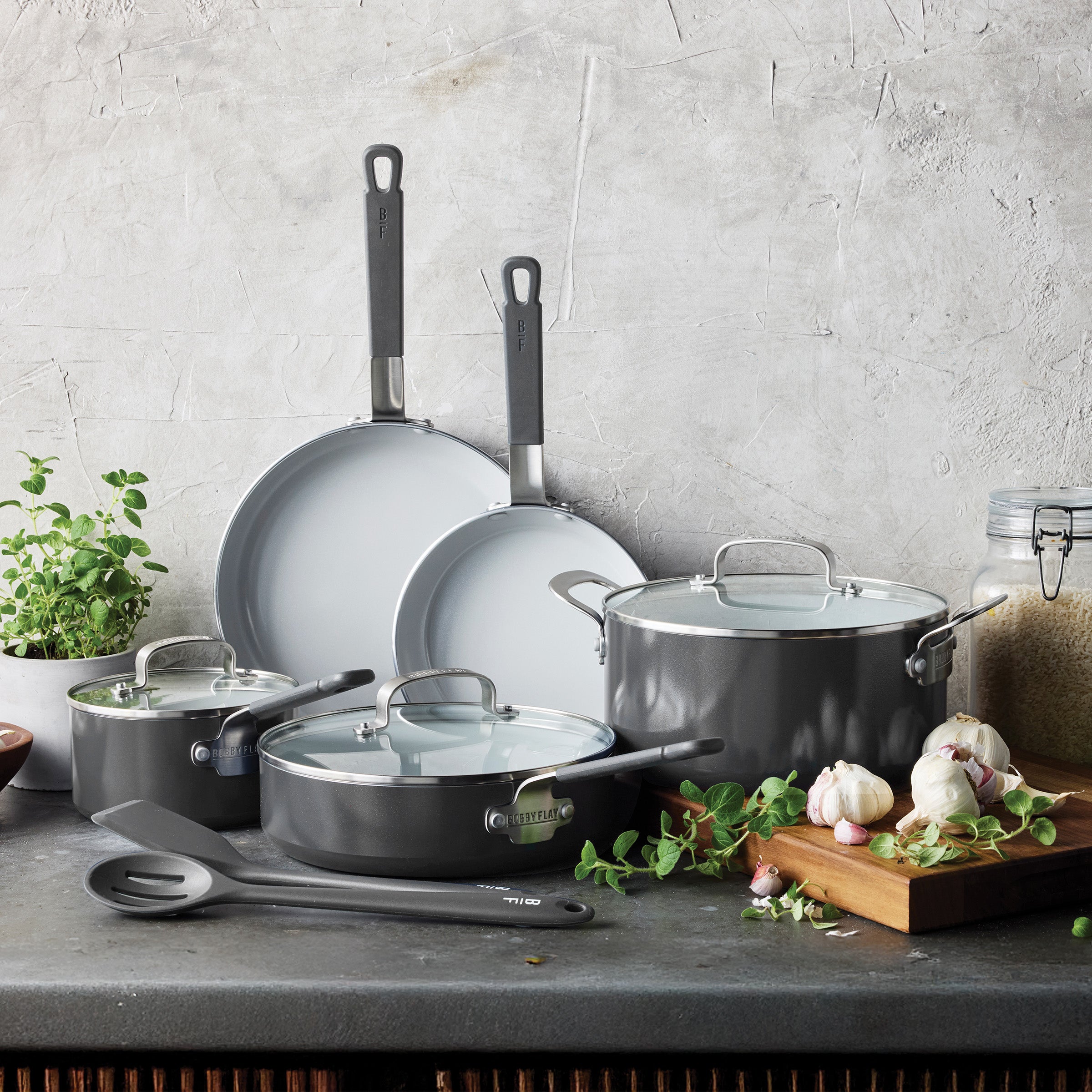 Graphite ceramic nonstick 10-piece cookware set on a counter with visible herbs and garlic.
