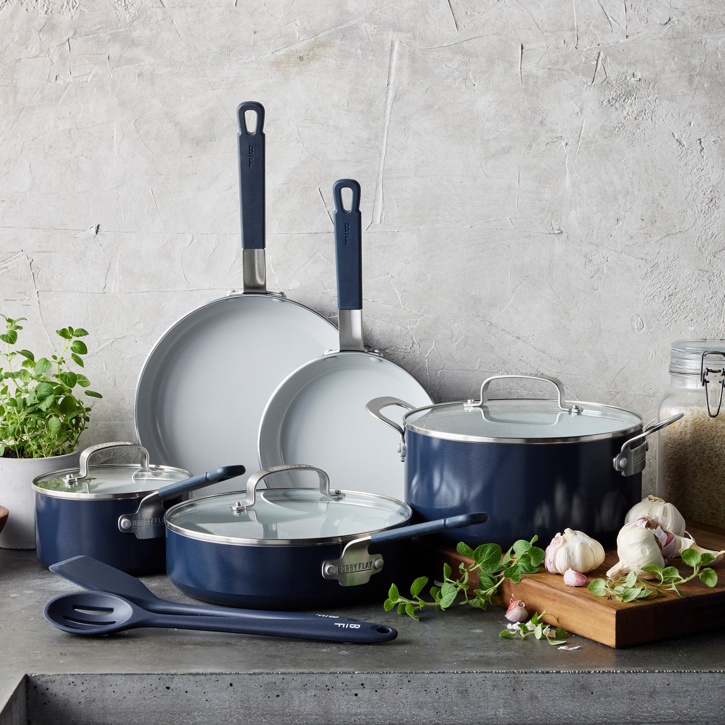 10-piece Oxford Blue cookware set with glass lids and utensils on a kitchen counter next to herbs and garlic.