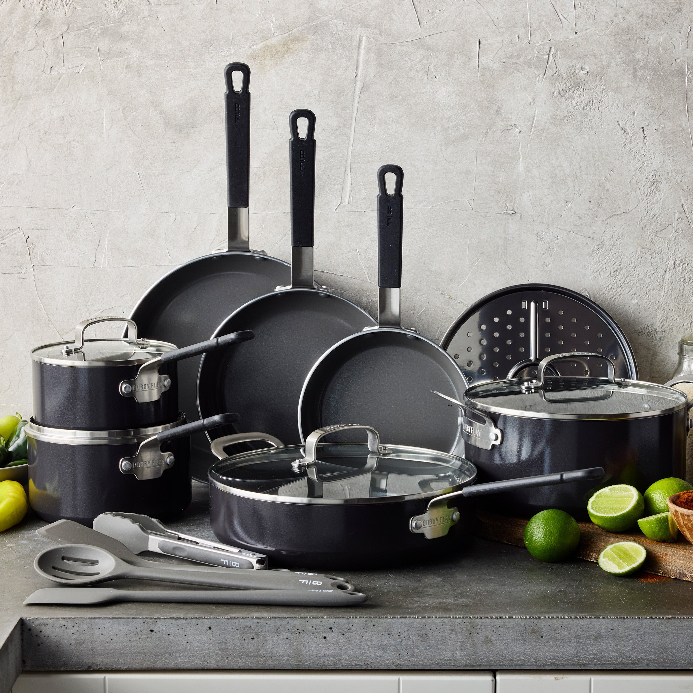 Black 16-piece nonstick cookware set on a counter with cut limes, modern design visible.